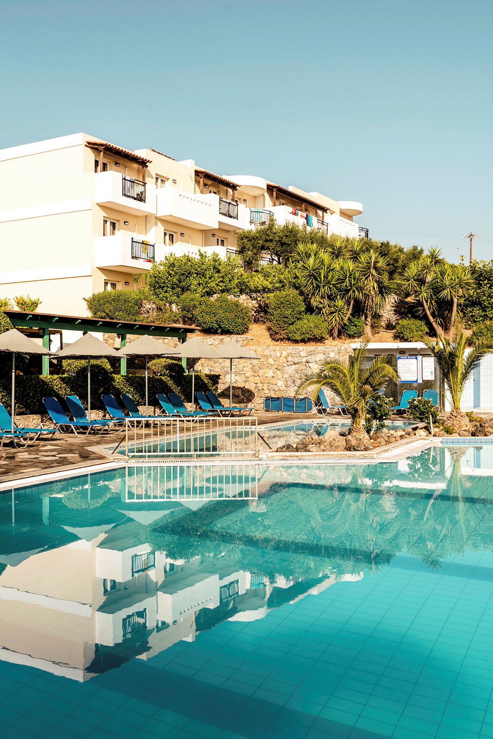 En bild av en hotellpool med solstolar och byggnader i bakgrunden. (AI-genererad text)