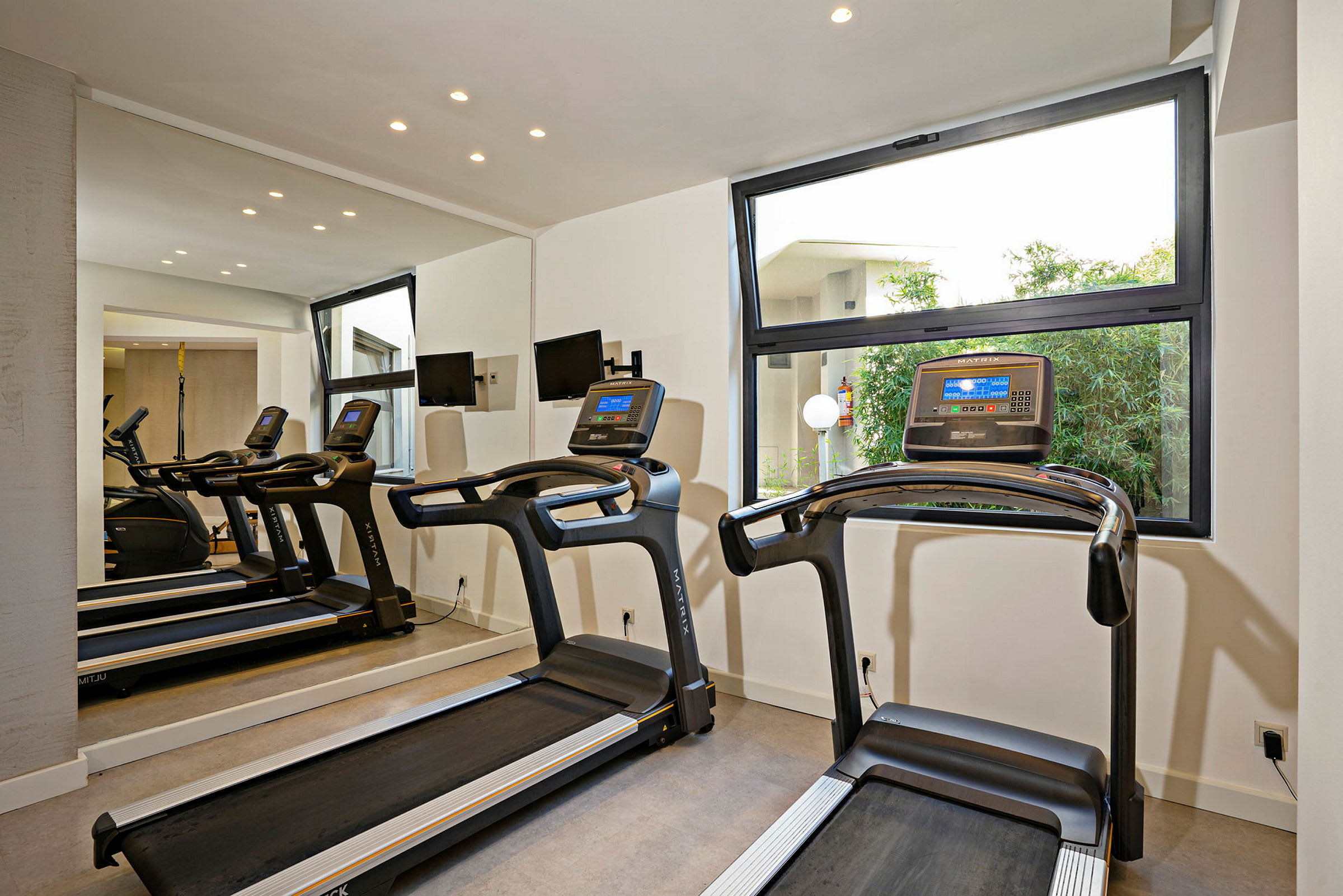 Två löpband i ett gym med stora fönster. (AI-genererad text)