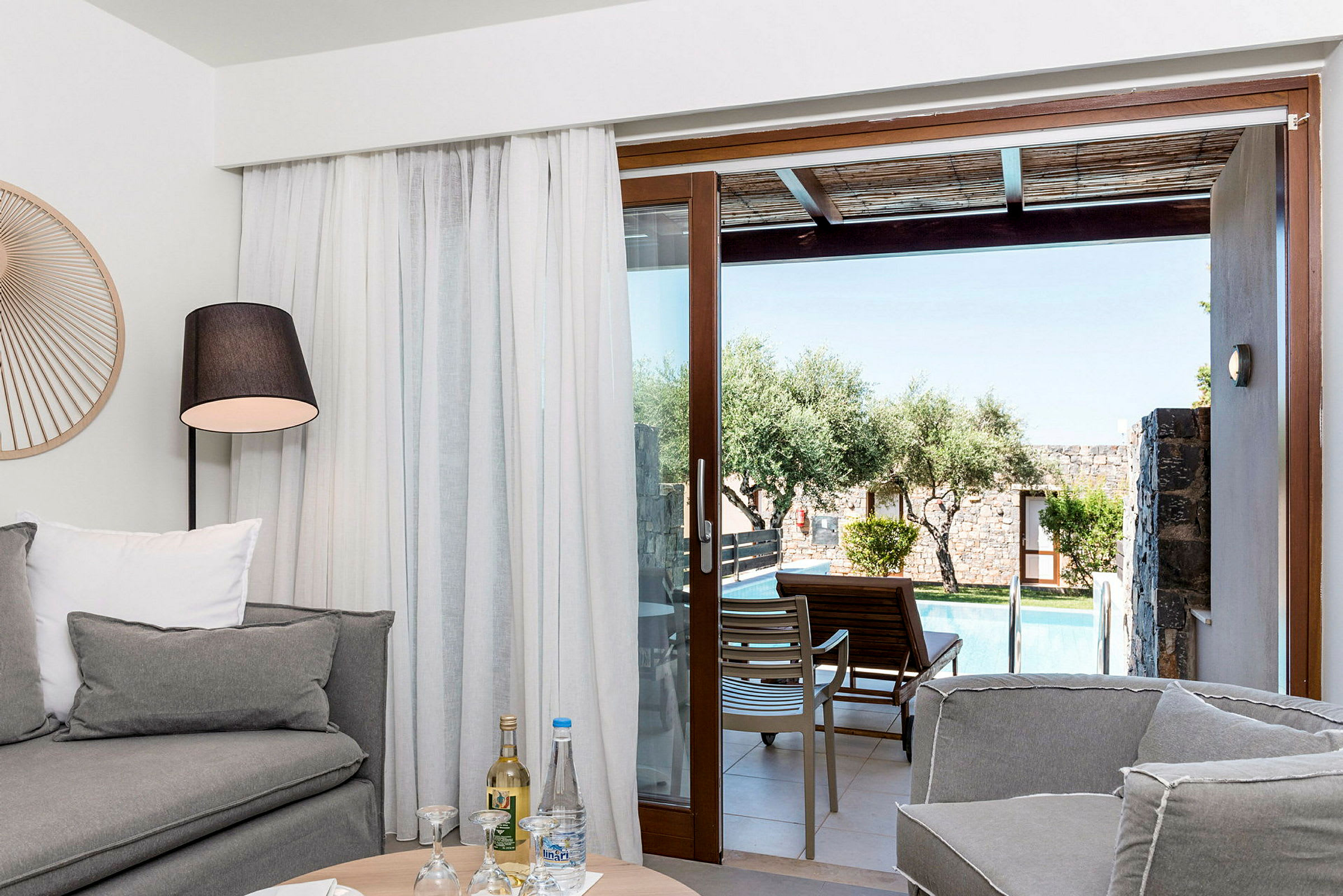 Ett vardagsrum med soffa och lampbord, med utsikt mot en uteplats med pool genom en glasdörr. (AI-genererad text)