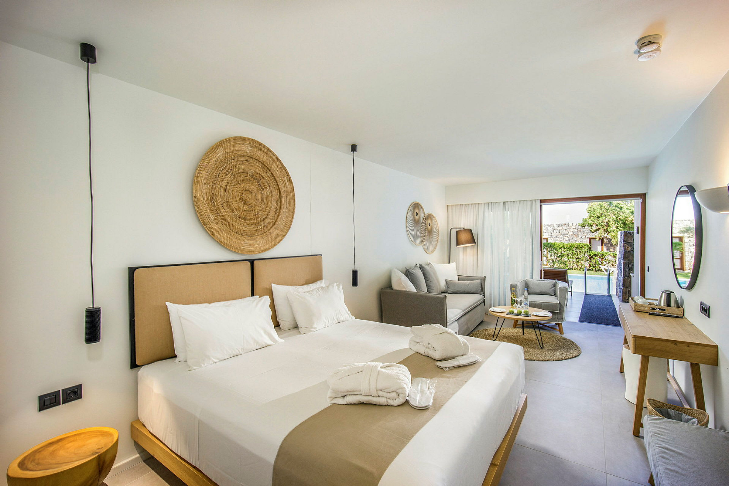 Ett modernt hotellrum med en stor säng, sittgrupp och en utsikt över en pool genom glasdörrar. (AI-genererad text)