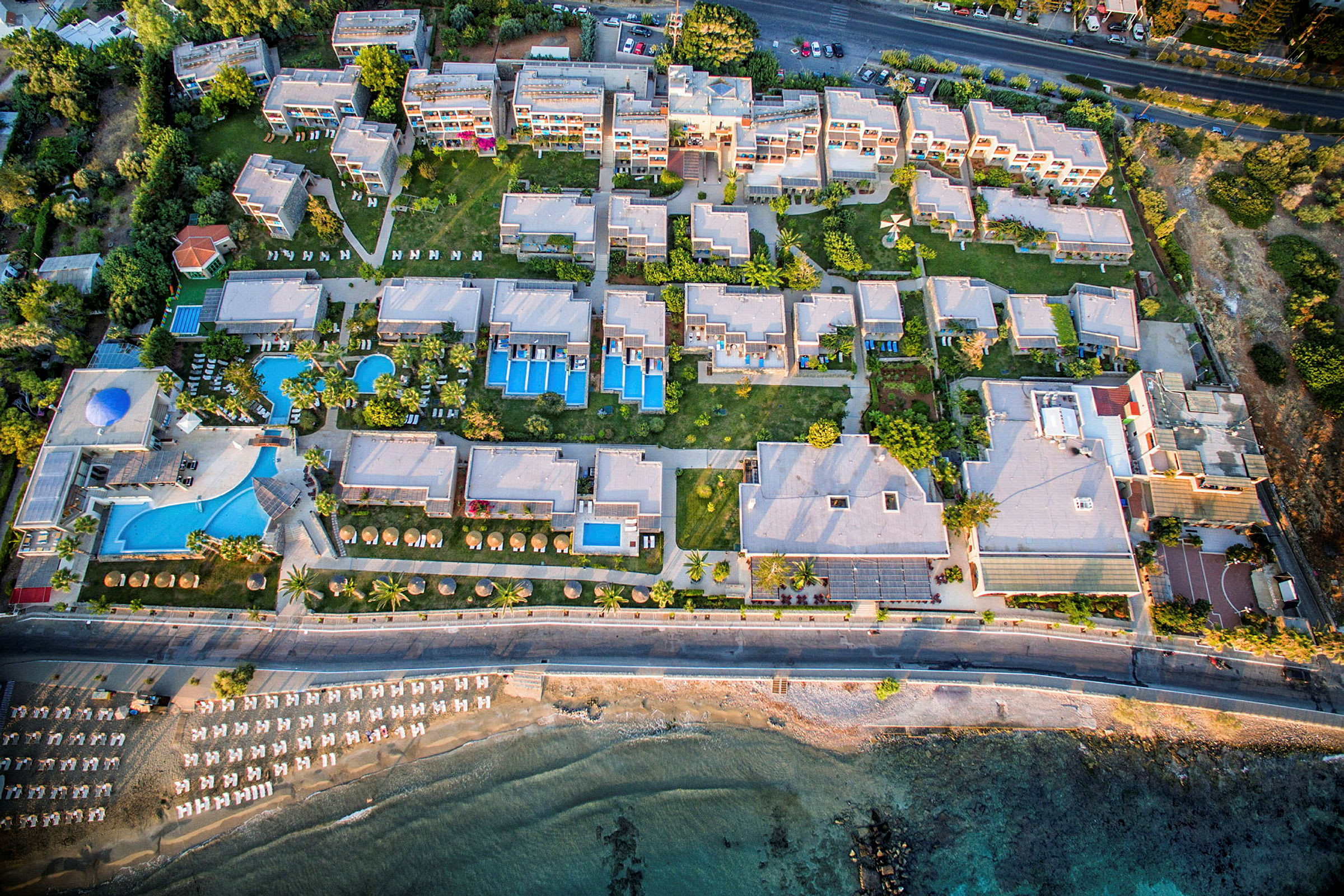 Flygfoto av ett semesterhotell med pooler, byggnader och strand. (AI-genererad text)