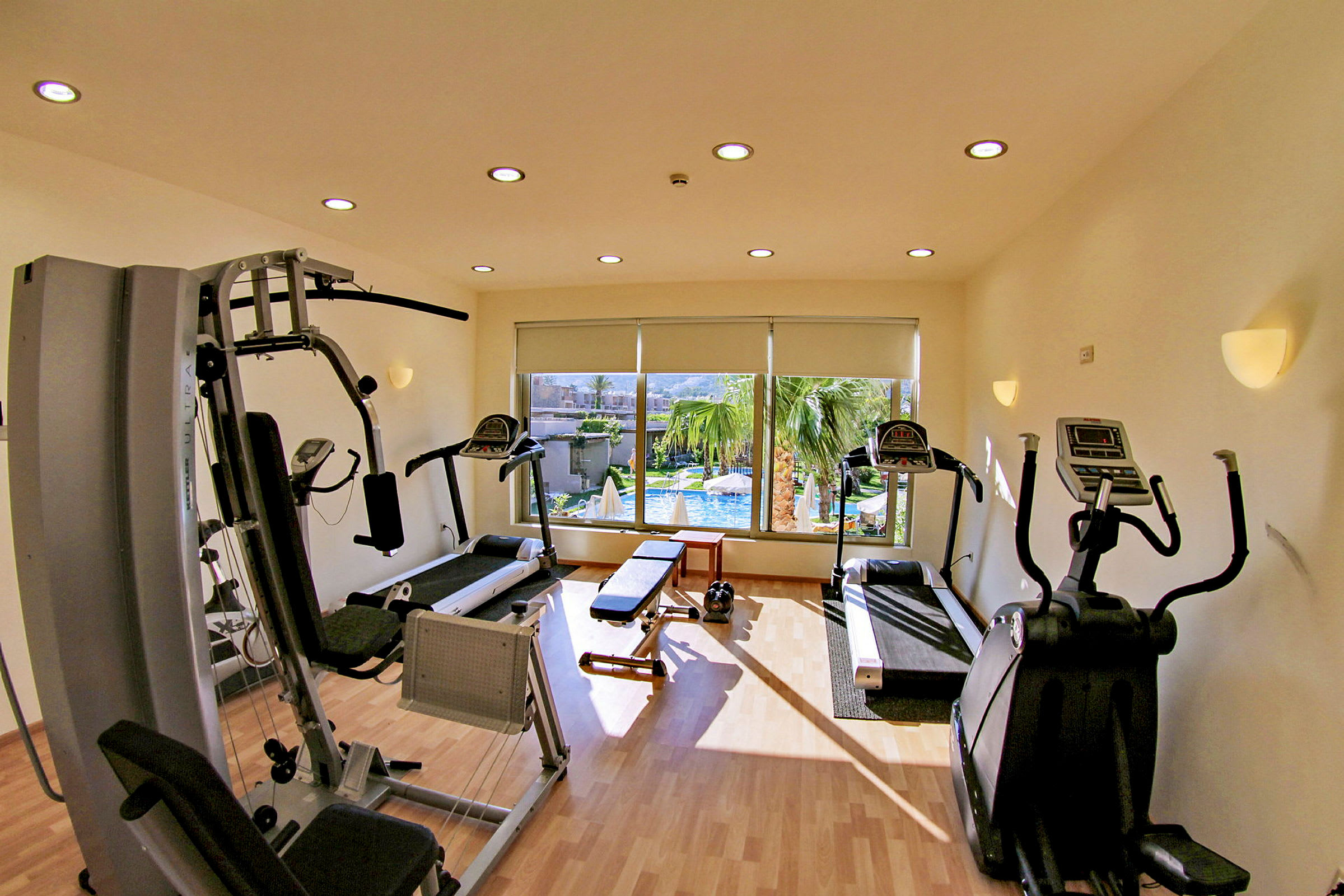 Ett gym med träningsutrustning och fönster med utsikt över poolområde. (AI-genererad text)