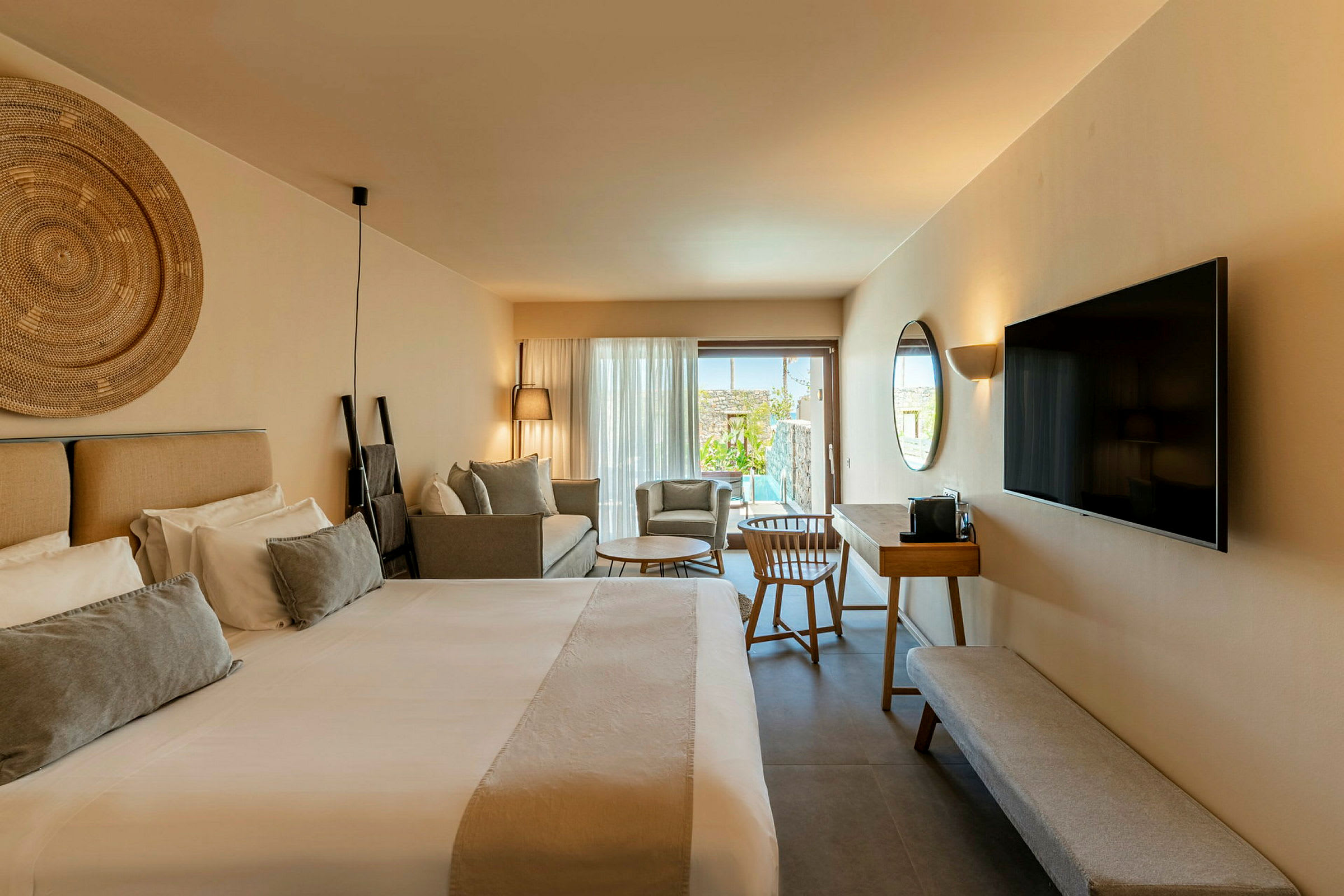 Ett modernt hotellrum med en stor säng, en soffa, en TV på väggen och ett skrivbord med stol. Rummet har en uteplats med poolutsikt. (AI-genererad text)