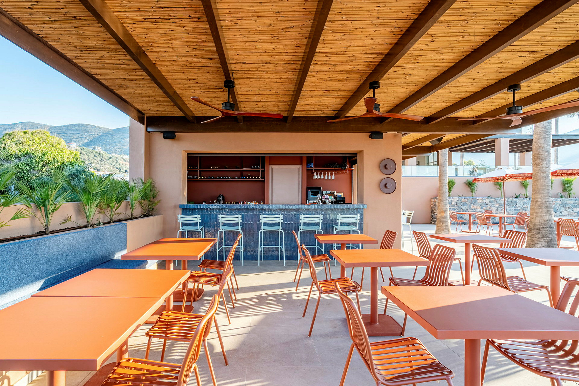 Restaurang eller bar med orange bord och stolar under ett tak vid en utomhusmiljö. (AI-genererad text)