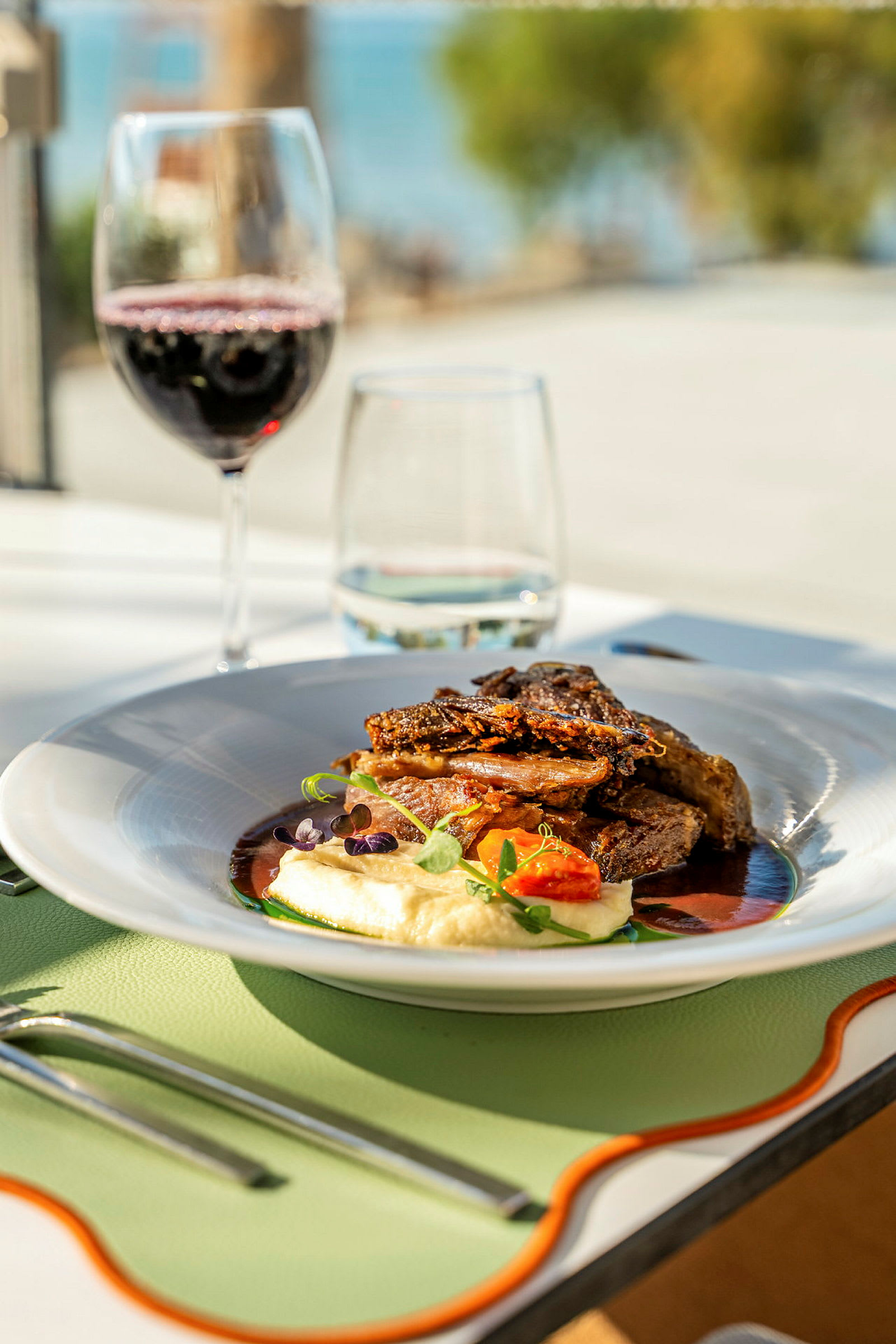 En tallrik med en gourmeträtt som innehåller kött, potatismos och grönsaker, samt ett glas rött vin på ett dukat bord. (AI-genererad text)