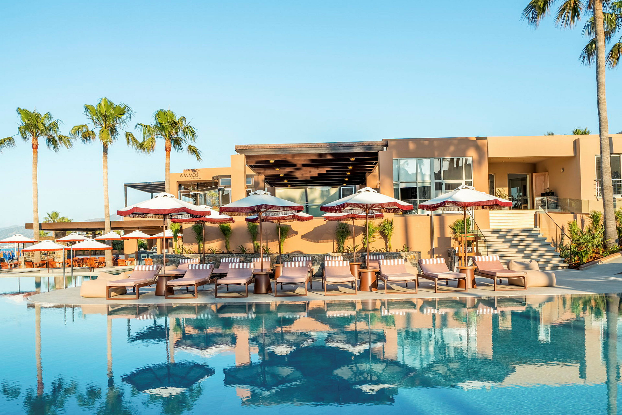 En pool med solstolar och paraplyer framför en modern byggnad. (AI-genererad text)