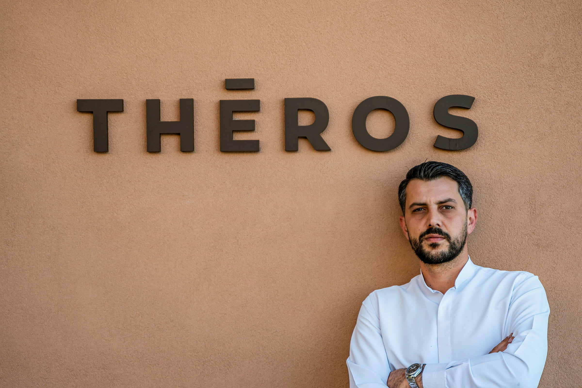 Man framför en vägg med texten "THÉROS". (AI-genererad text)