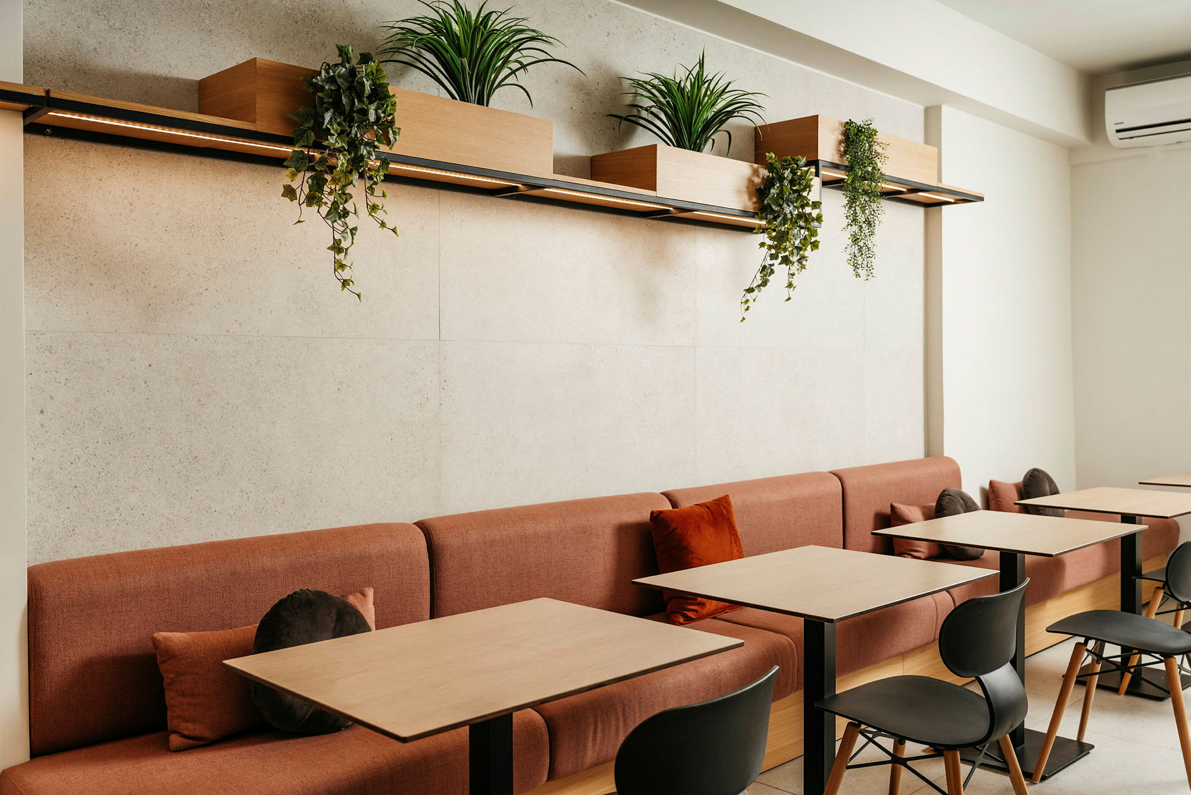 Ett modernt caféområde med röda soffor och träbord, dekorerat med växtlådor hängande ovanför. (AI-genererad text)