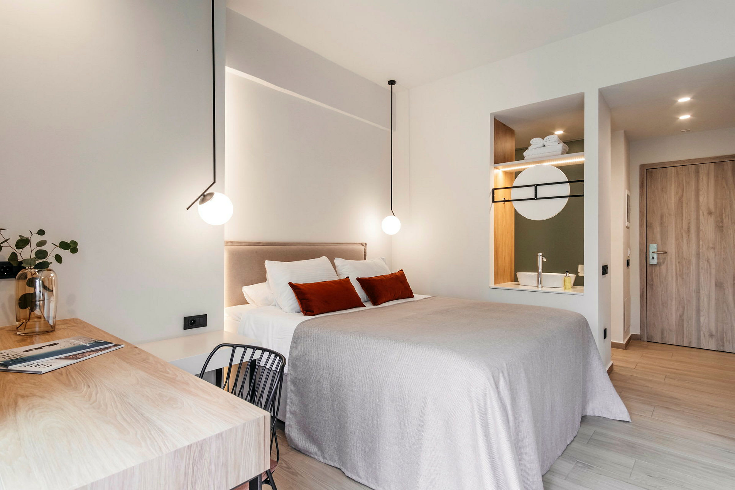 Ett modernt inrett hotellrum med en dubbelsäng, skrivbord och integrerat handfat med spegel. (AI-genererad text)