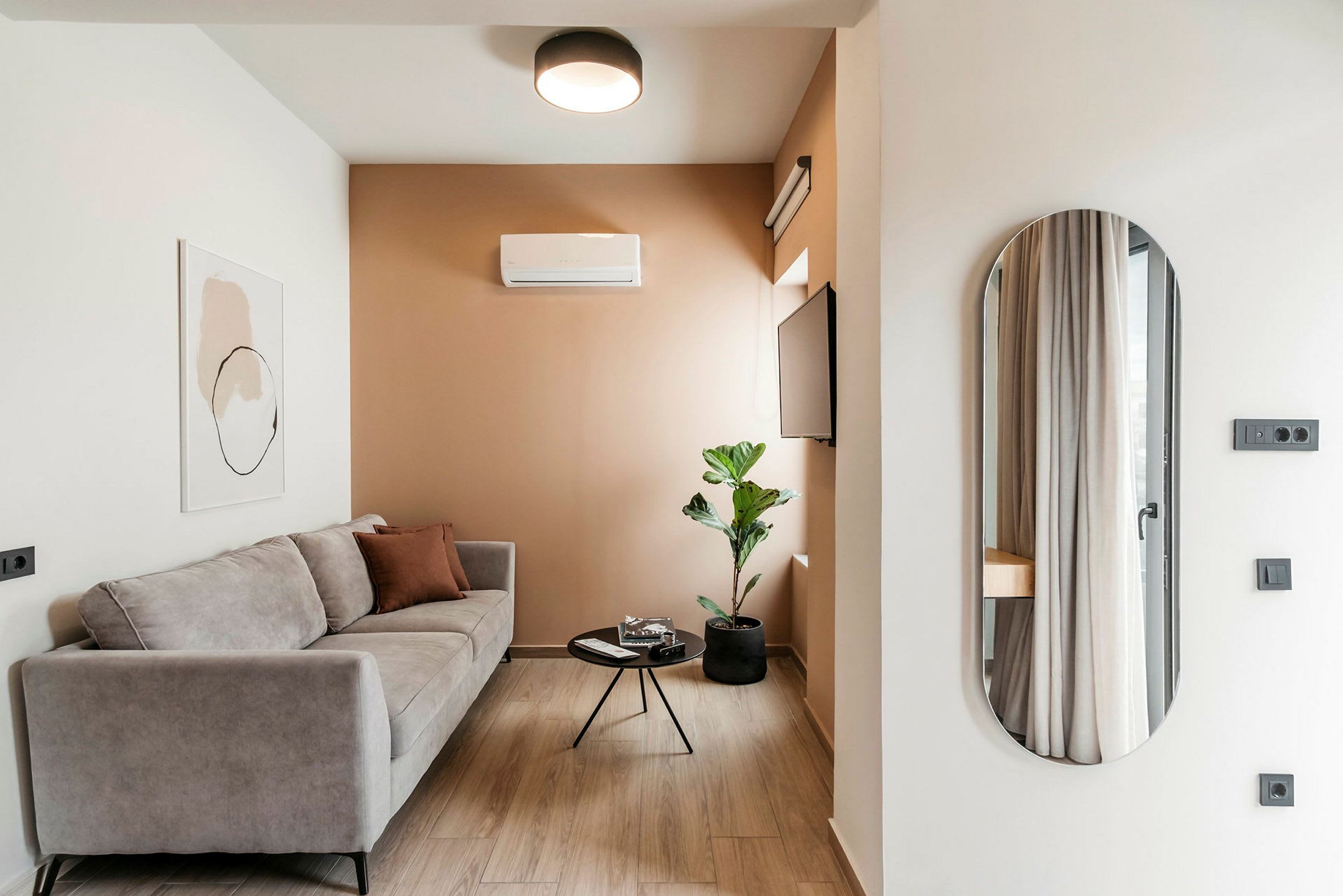 Ett modernt vardagsrum med en grå soffa, ett litet runt soffbord, en växt i kruka och en väggmonterad TV. (AI-genererad text)