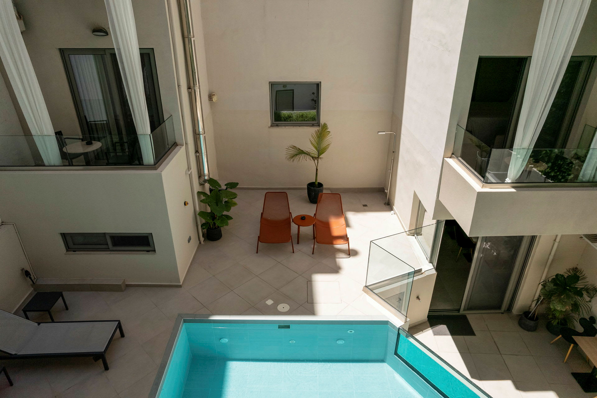 Bild av en innergård med solstolar, ett bord och en pool. Växter och glasräcken skapar en modern känsla. (AI-genererad text)