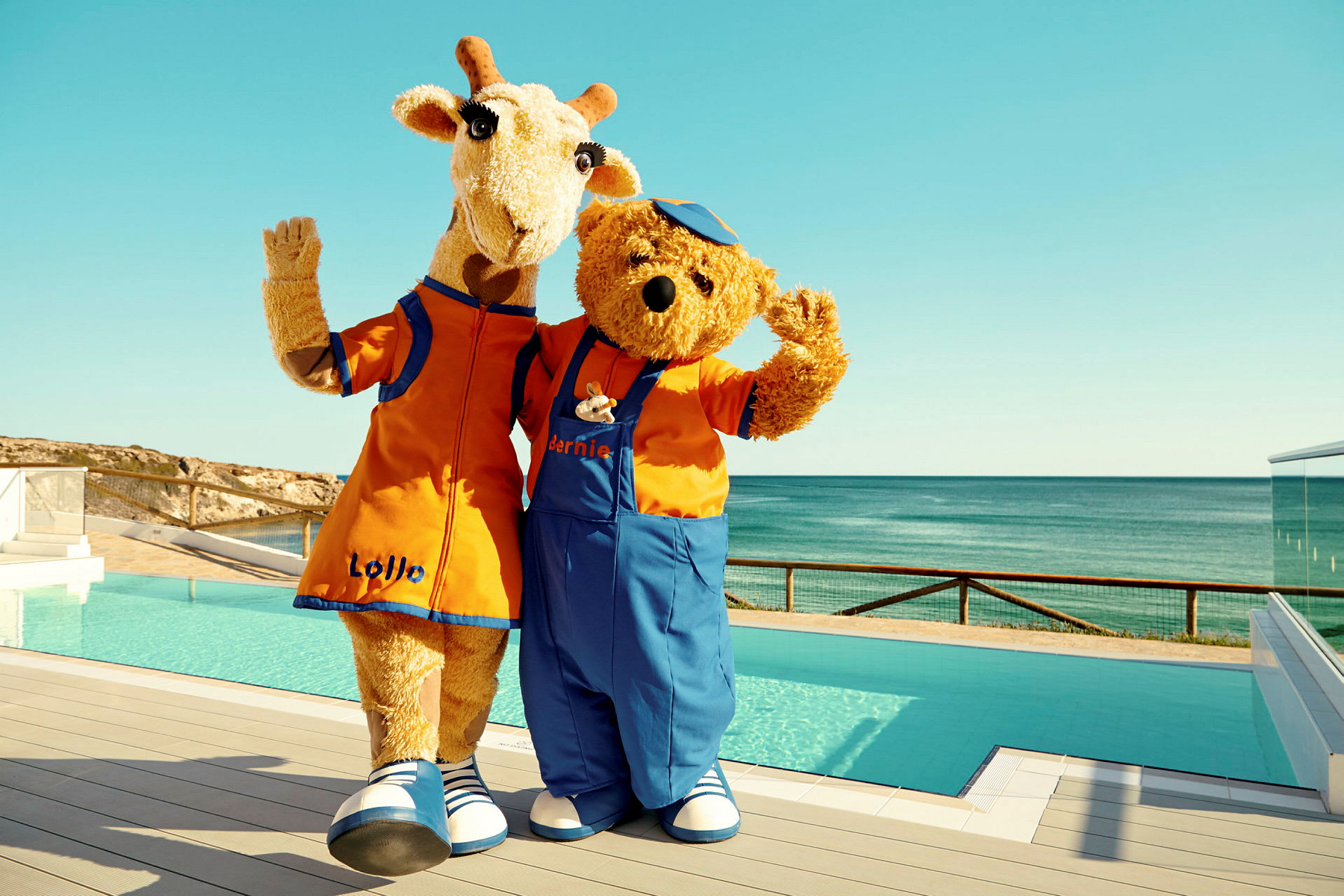Två maskotar, en giraff och en björn, står vid en pool och vinkar. (AI-genererad text)