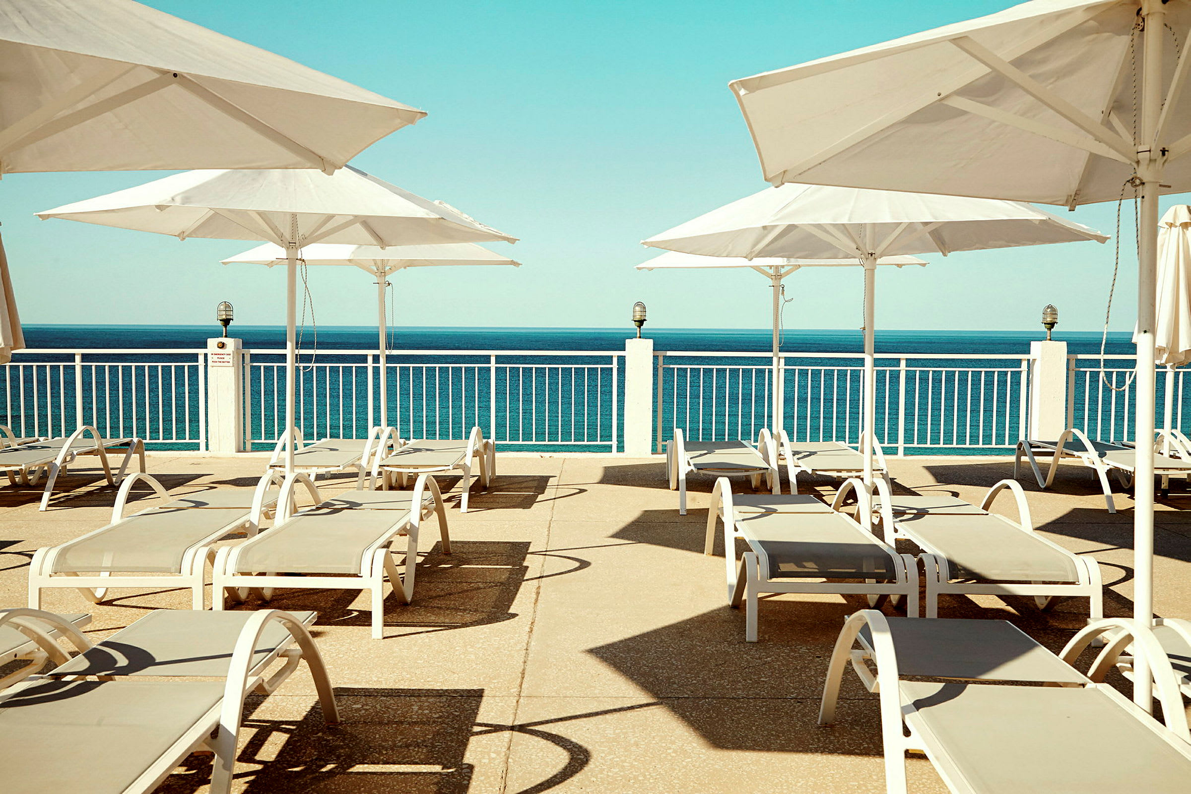 Utsikt över en solterrass med solstolar och parasoller, med havet i bakgrunden. (AI-genererad text)