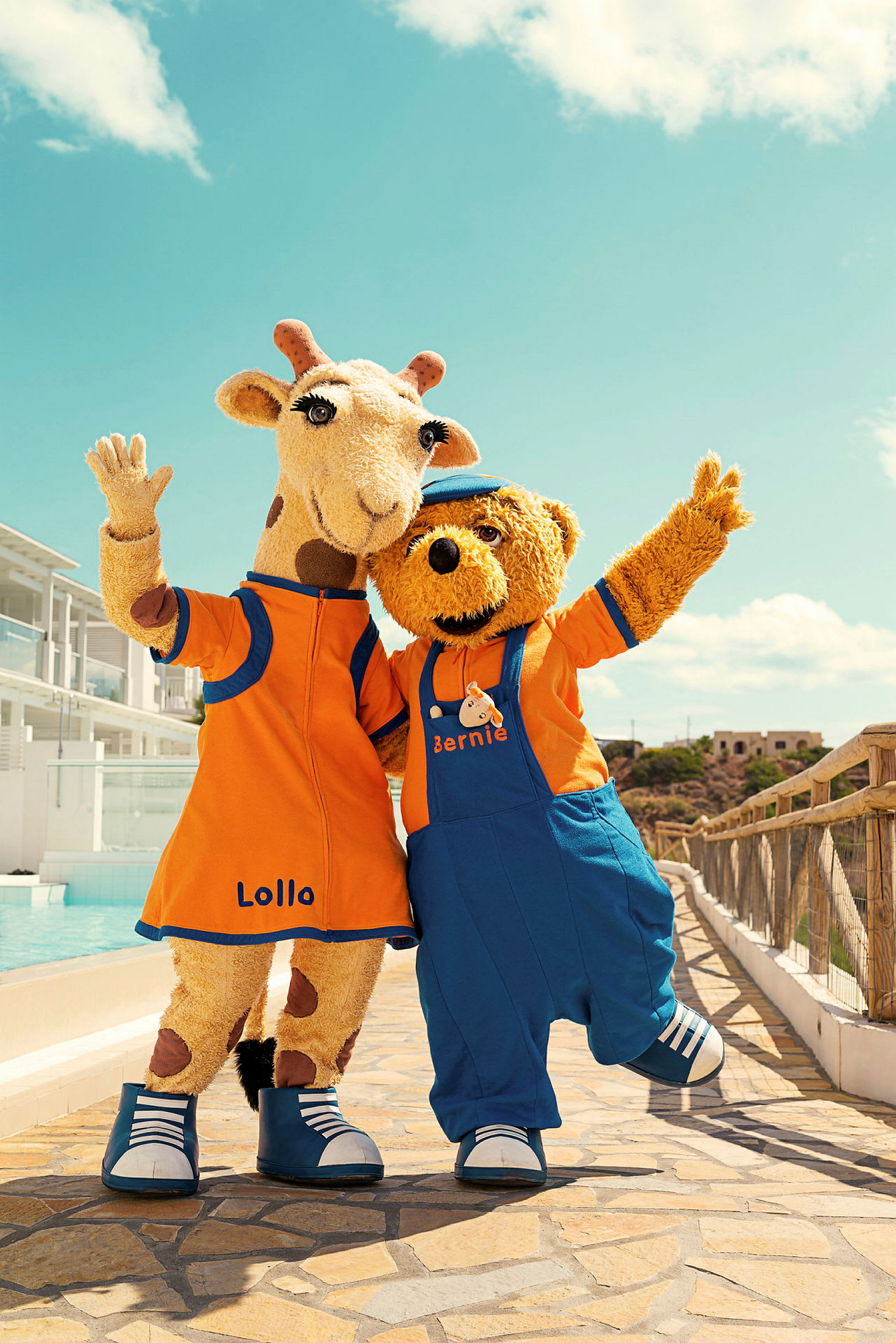 Två maskotfigurer, en giraff och en björn, står bredvid varandra vid en pool och vinkar. (AI-genererad text)