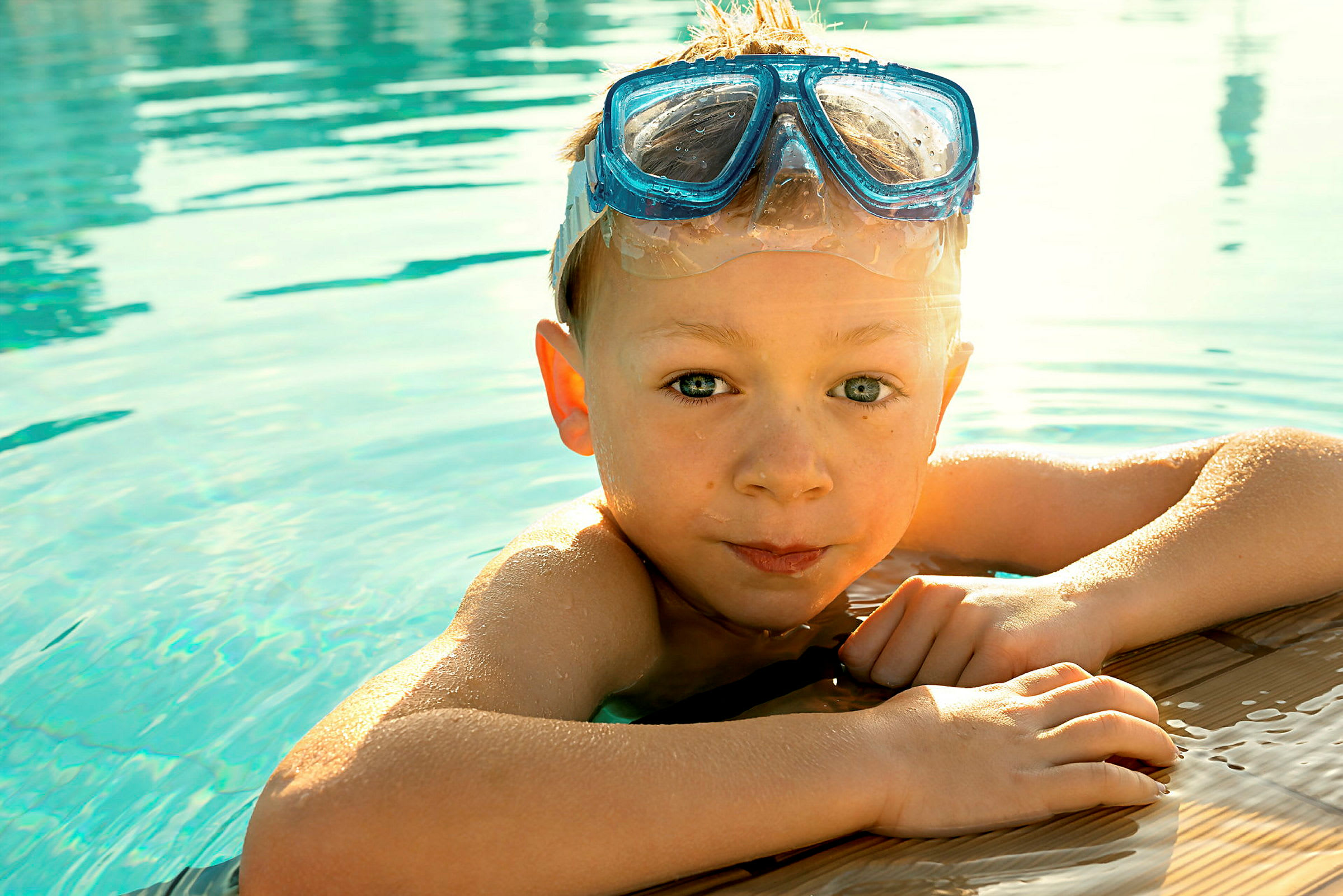 Ett barn håller i kanten av en pool och har på sig ett par blå snorkelglas. (AI-genererad text)