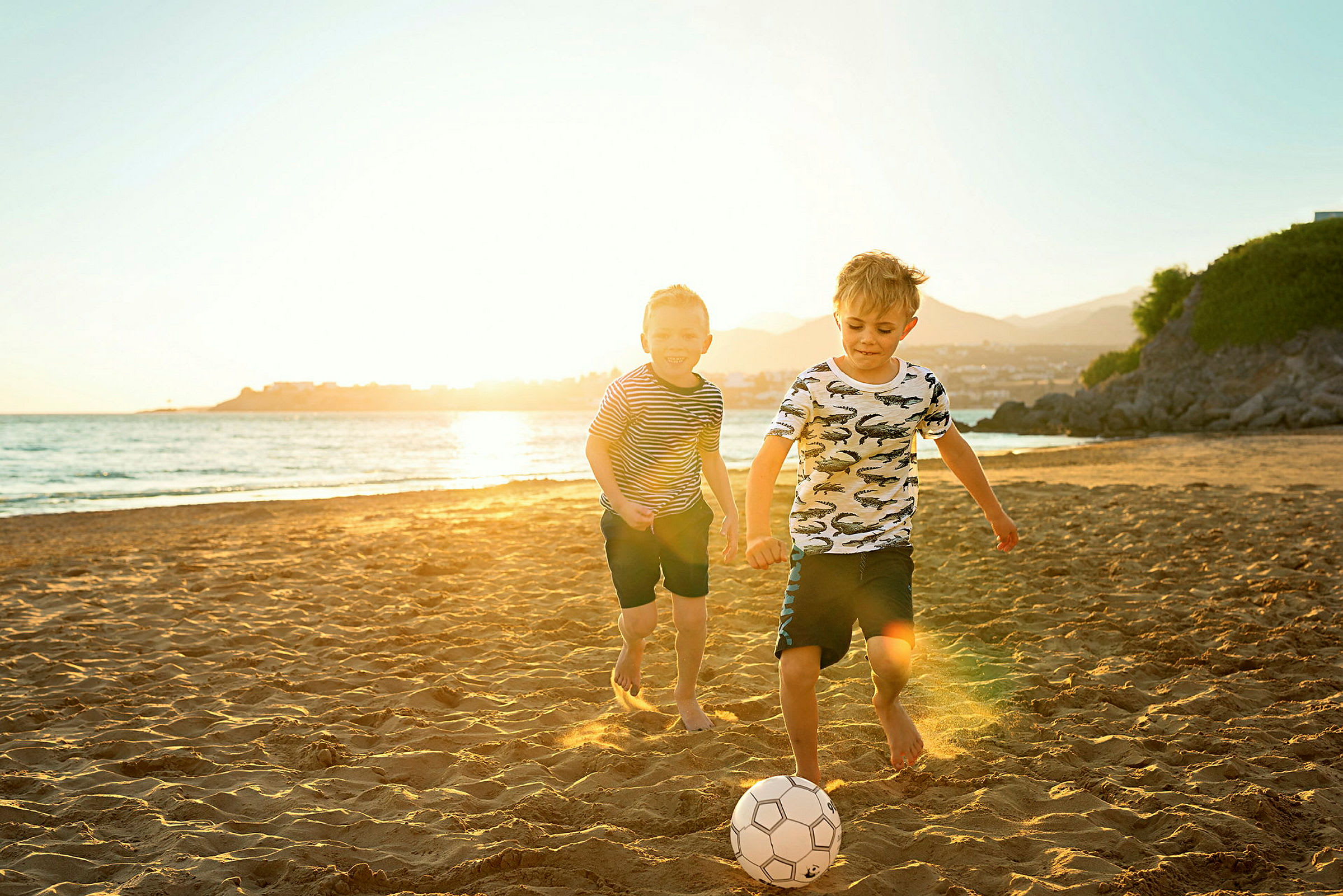 Två barn spelar fotboll på en solig strand. (AI-genererad text)