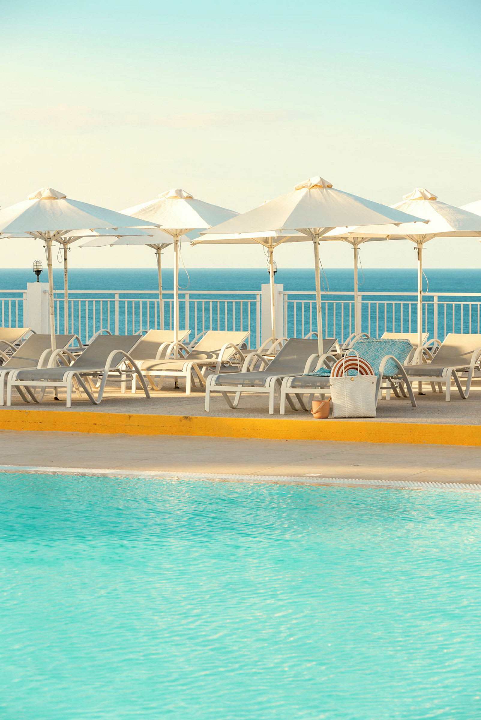Solstolar och parasoller vid en pool, med havet i bakgrunden. (AI-genererad text)