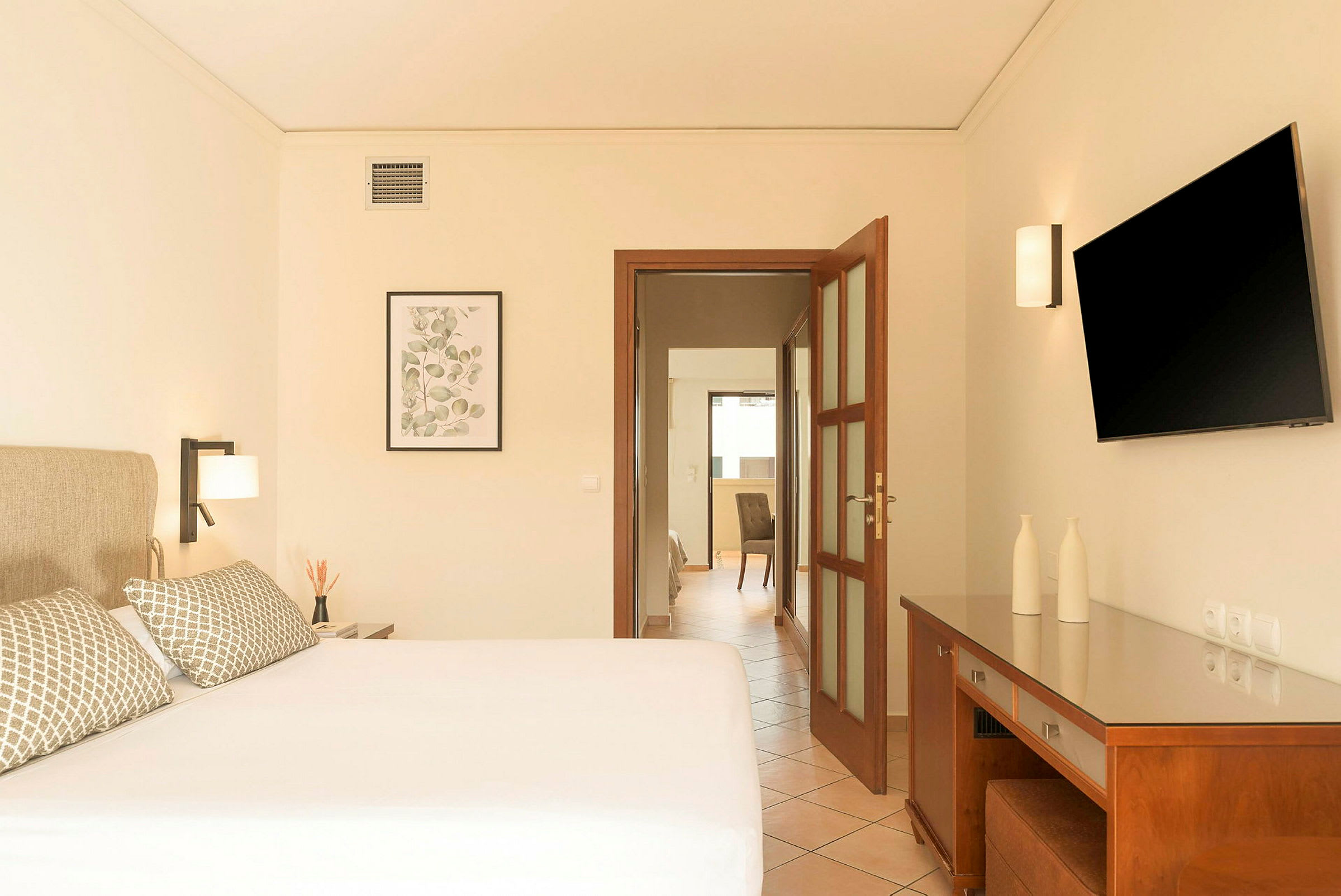 Hotellrum med en dubbelsäng, sänglampor, en väggmonterad TV och ett skrivbord med dekorativa föremål. (AI-genererad text)
