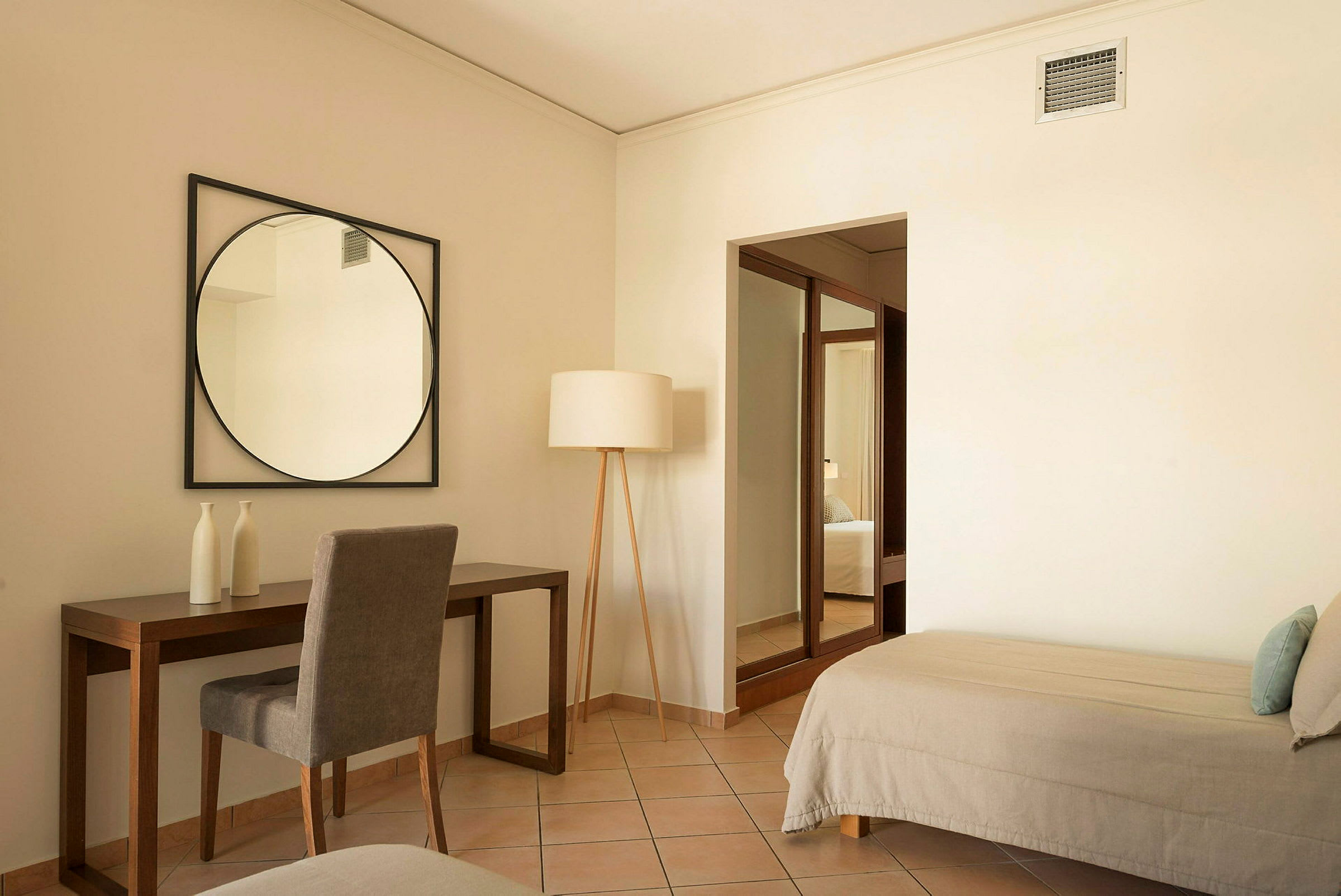 Ett hotellrum med skrivbord, stol och spegel samt en säng och en golvlampa. (AI-genererad text)