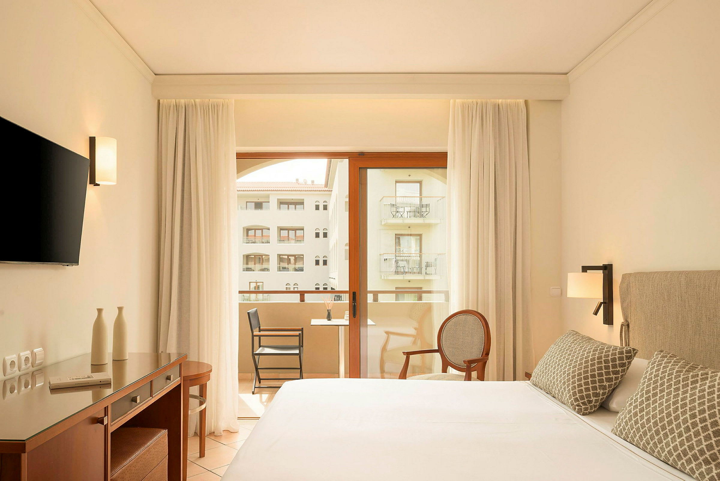 Modernt hotellrum med dubbelsäng, skrivbord, TV och balkong med utsikt. (AI-genererad text)
