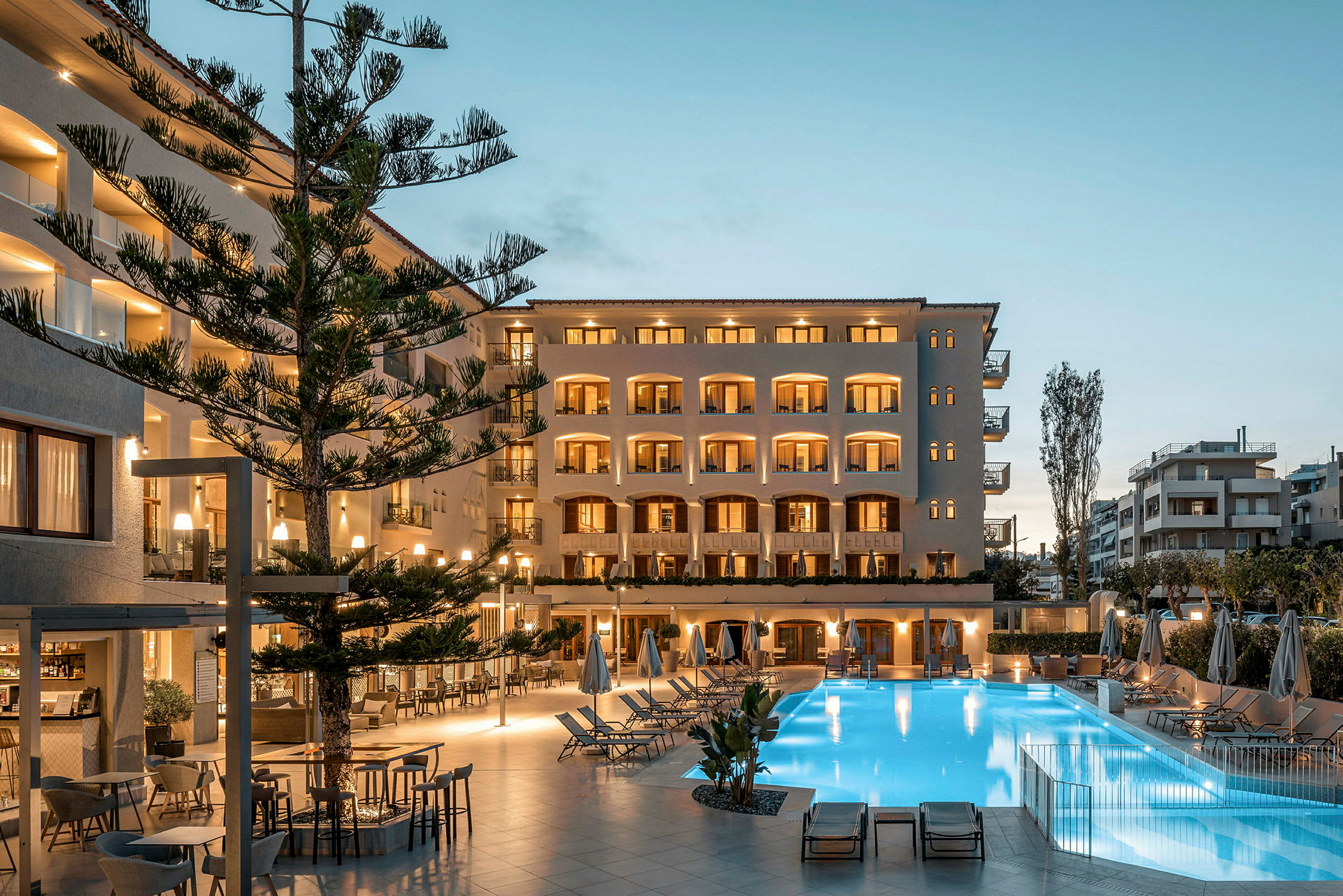 Utsikt över en upplyst hotellfasad med balkonger framför en pool och uteplats på kvällen. (AI-genererad text)