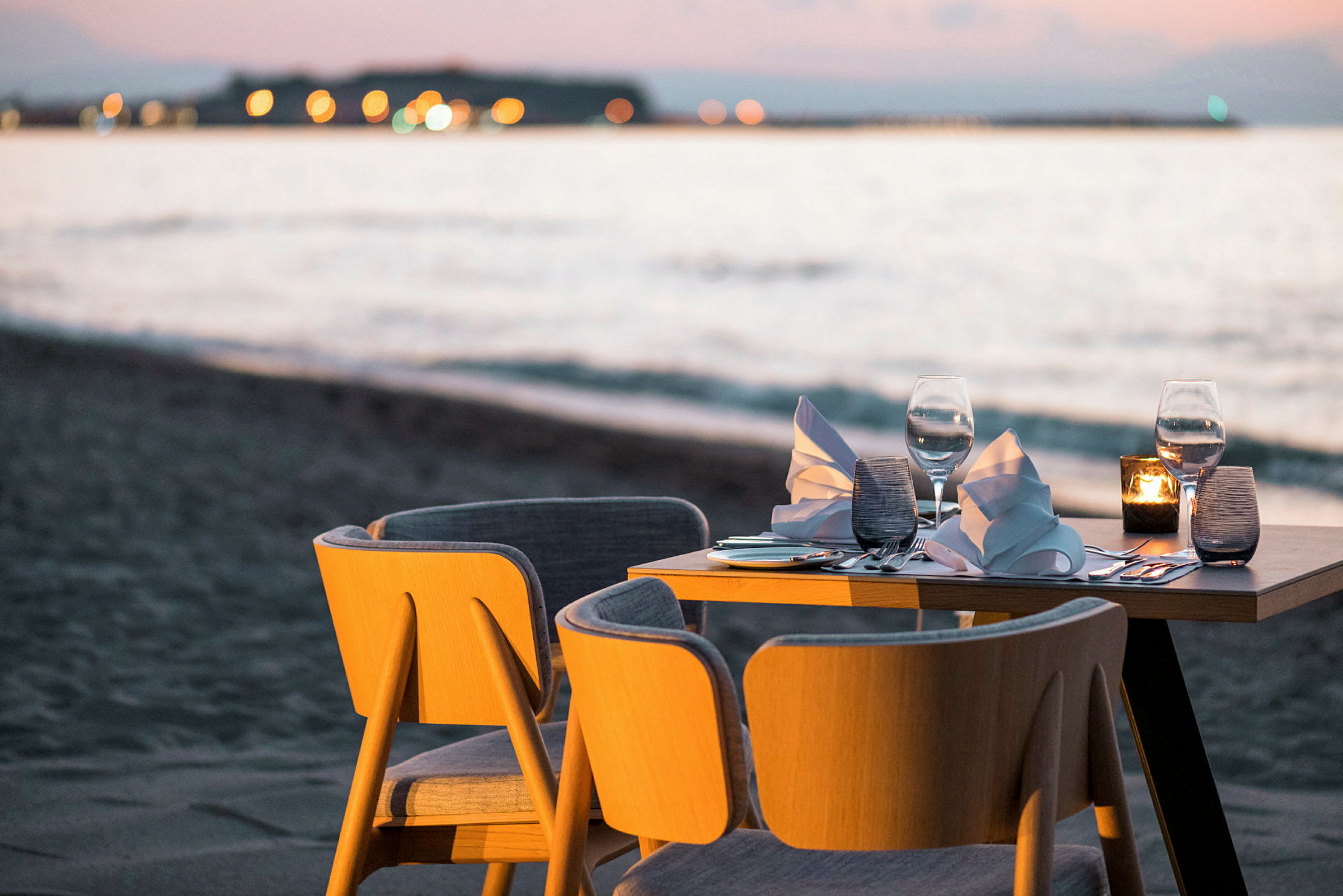 Ett dukat bord med två stolar vid stranden, i solnedgångens ljus. (AI-genererad text)