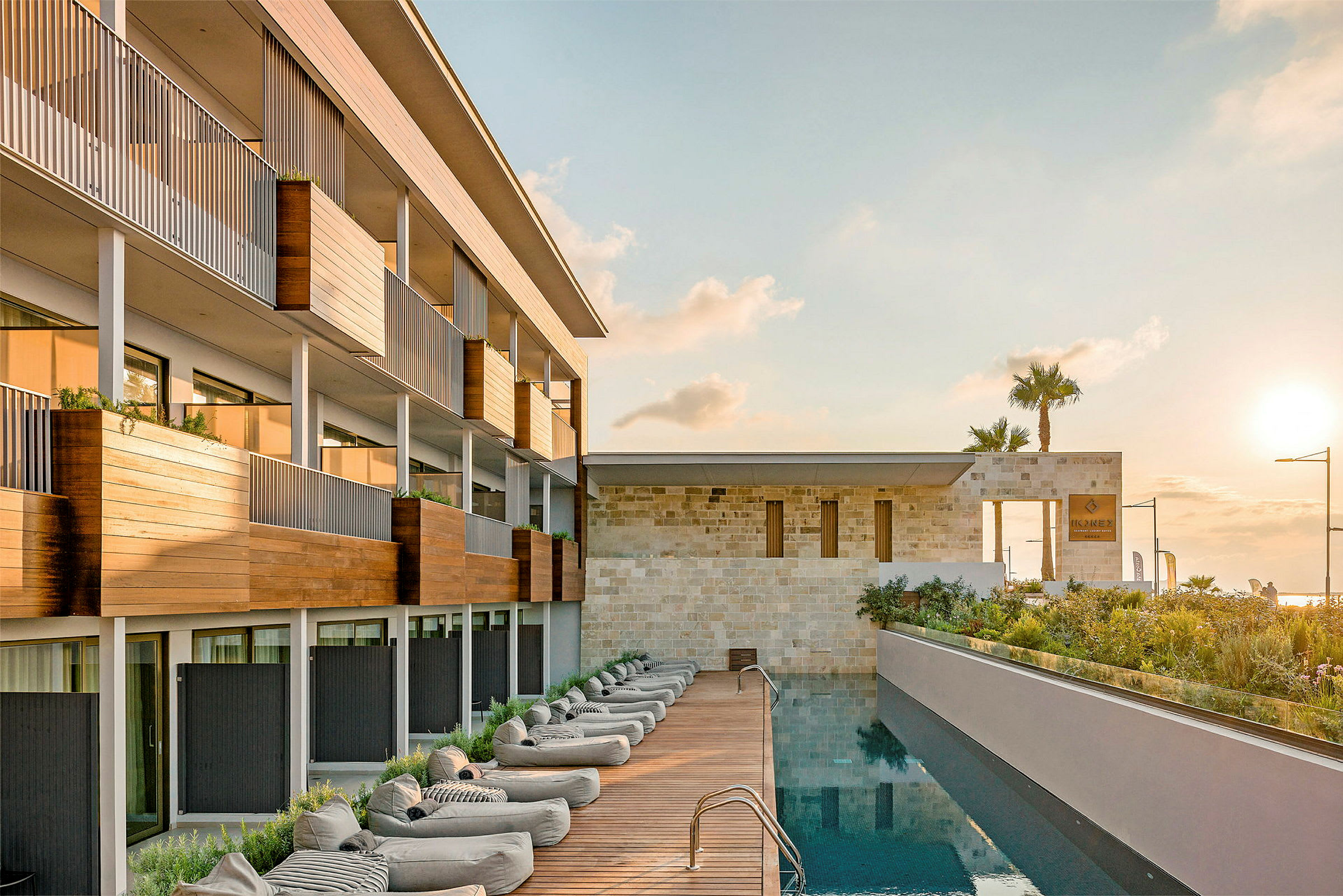 Modern hotellbyggnad med trädetaljer, pool, och loungemöbler vid solnedgång. (AI-genererad text)