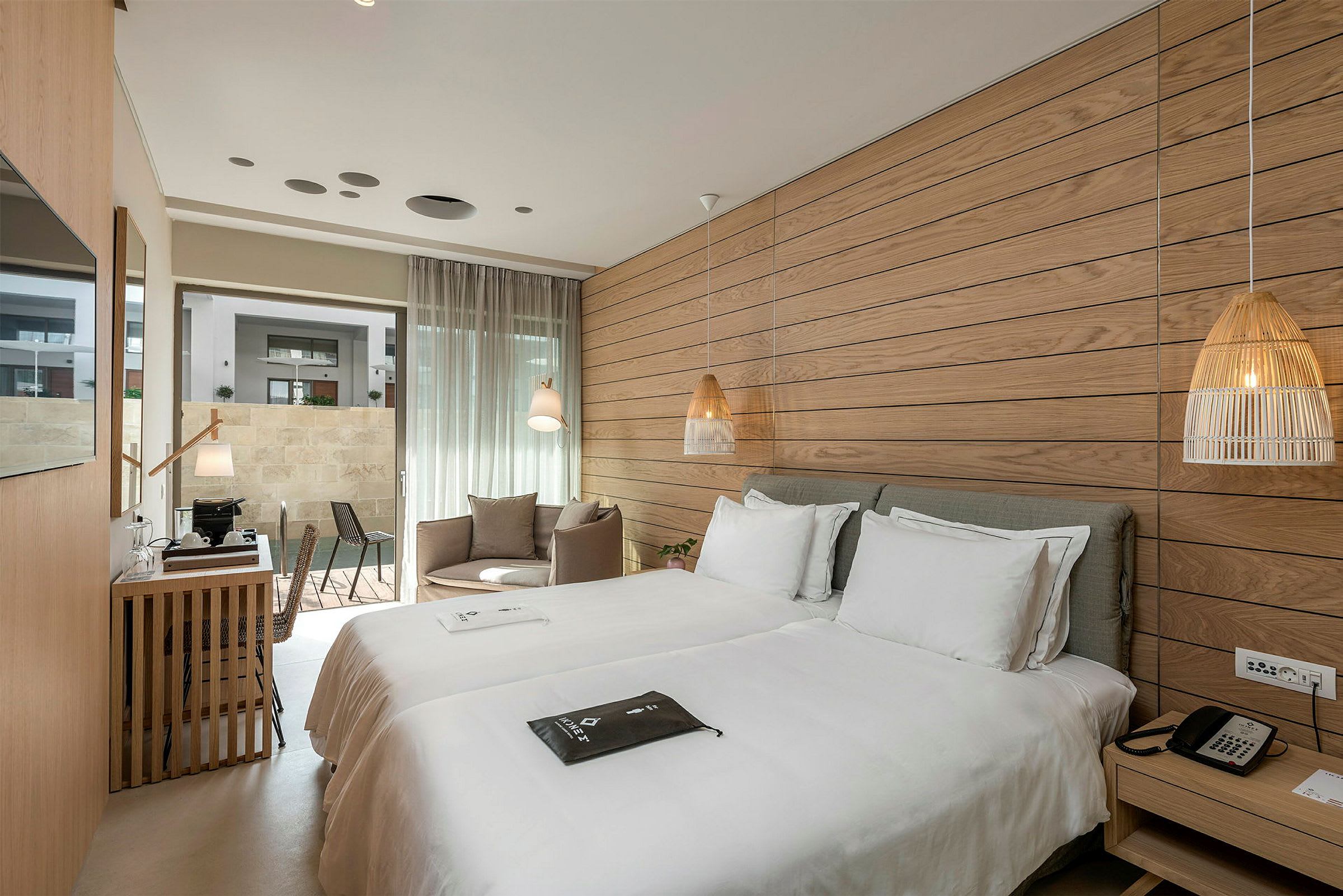 Ett hotellrum med två enkelsängar, en sittgrupp och ett skrivbord nära en glasdörr som leder till uteplatsen. (AI-genererad text)