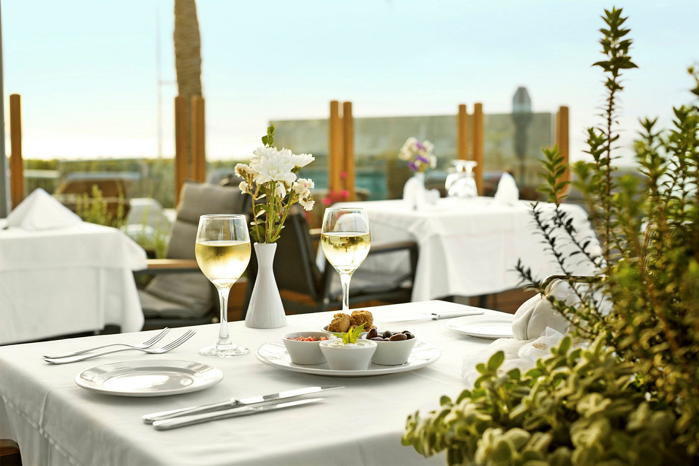 En dukad restaurangbord med ett glas vitt vin, blomdekoration och tallrik med tilltugg. (AI-genererad text)