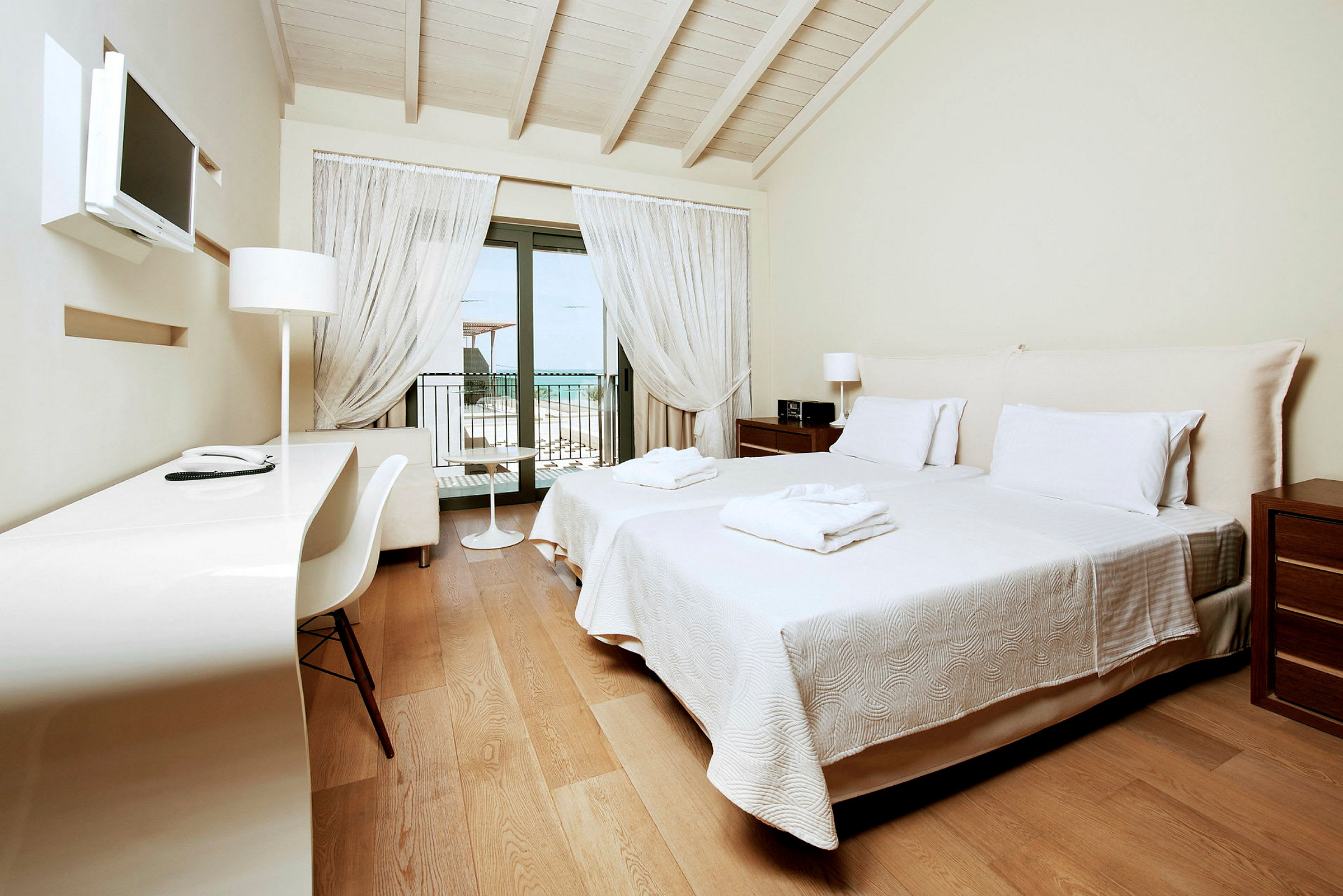 Ett hotellrum med två enkelsängar, ett skrivbord och en balkong med utsikt. (AI-genererad text)
