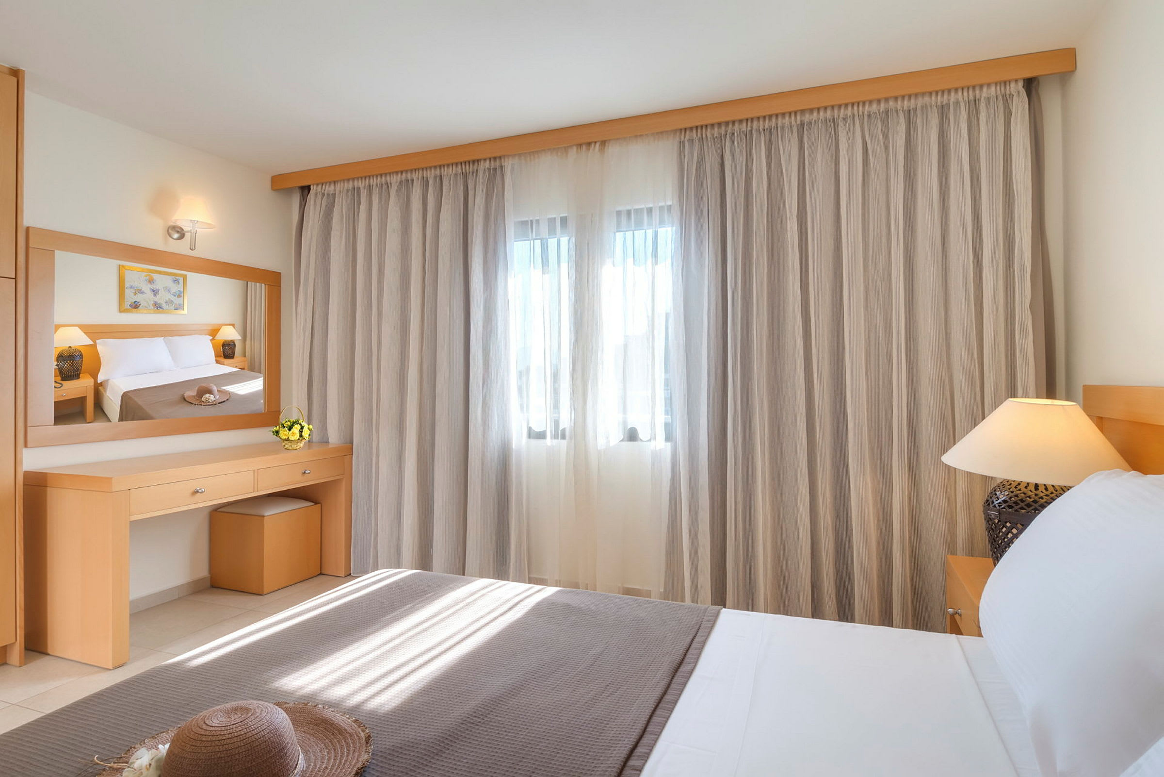 Ett hotellrum med en säng, en spegel och gardiner över ett fönster. (AI-genererad text)