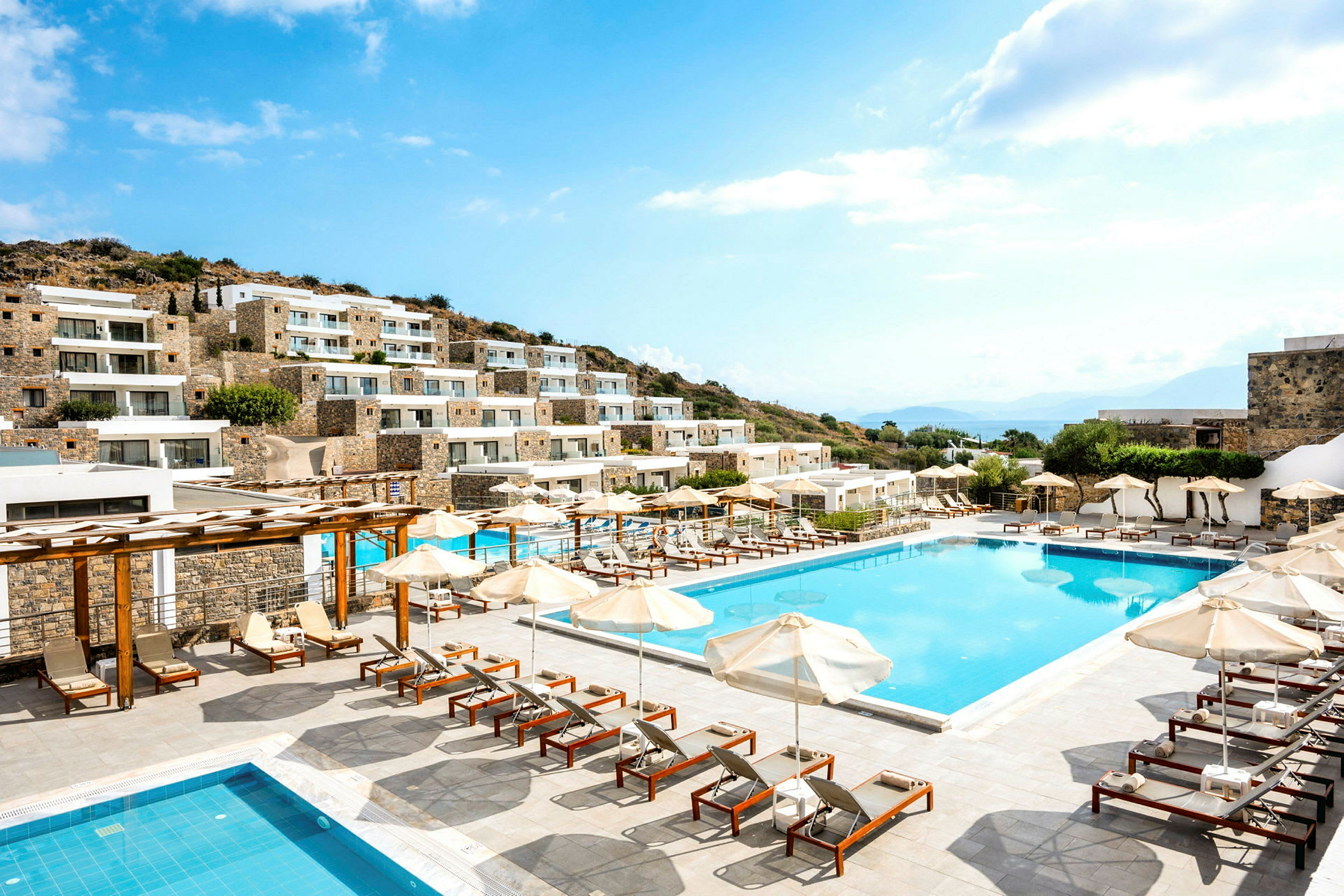 Bild av hotell med flera byggnader, pool och solstolar utomhus. (AI-genererad text)
