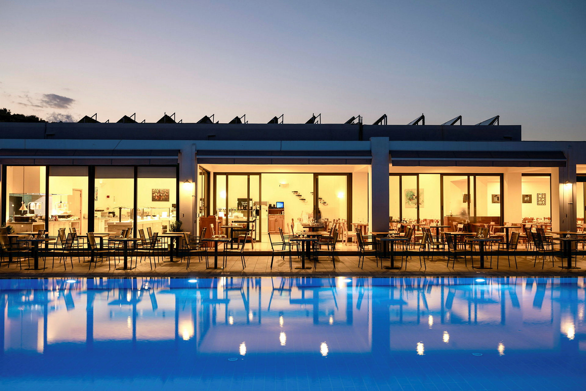 Hotellrestaurang med uteservering under kvällstid, med utsikt över en upplyst pool. (AI-genererad text)