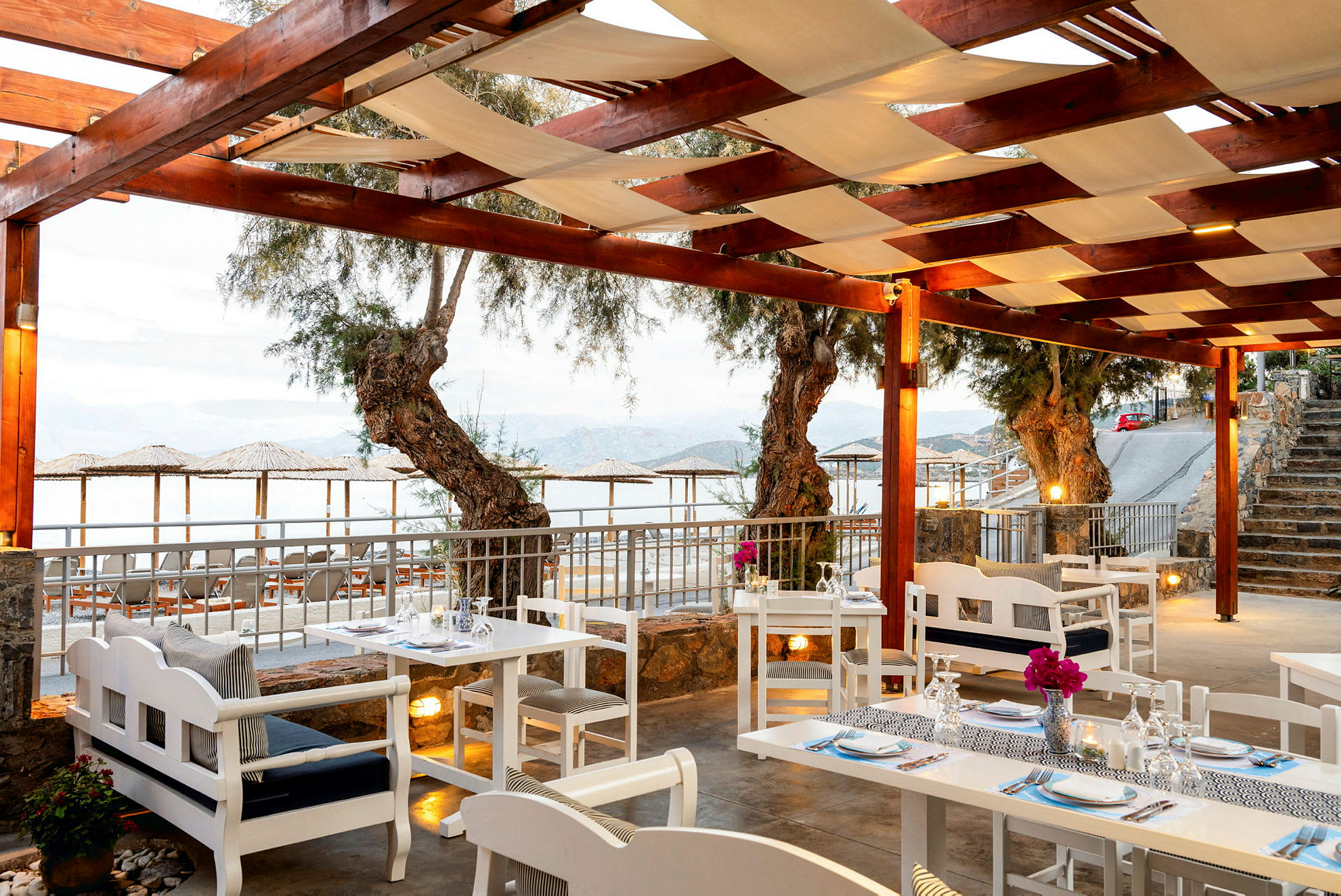 Restaurang med vita bord och stolar under ett träpergola med utsikt över havet. (AI-genererad text)
