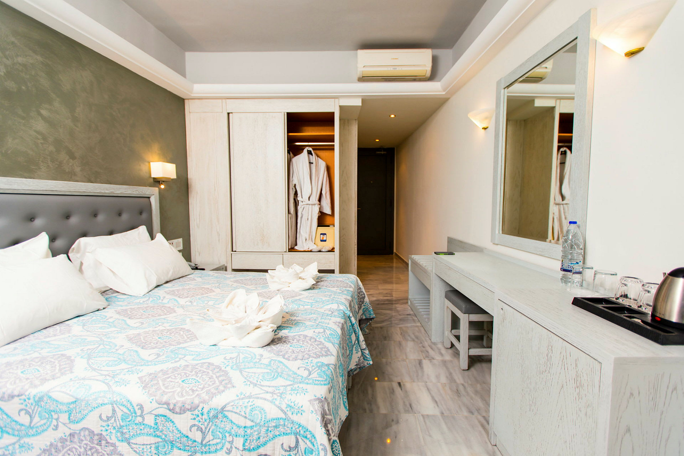Hotellrum med dubbelsäng, en spegel ovanför ett skrivbord och en öppen garderob med badrockar. (AI-genererad text)