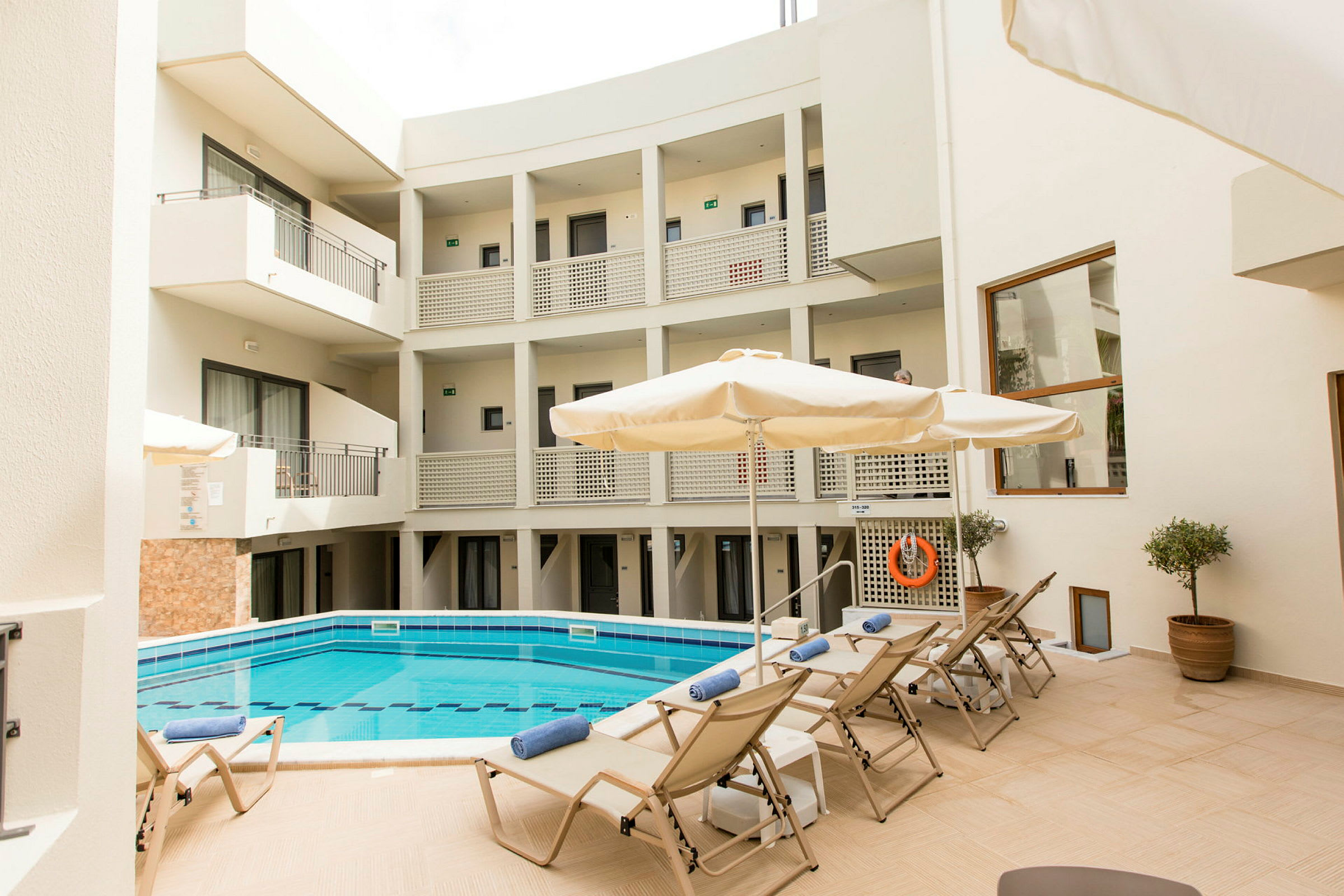 Innergård med en pool, solstolar och parasoller vid ett flerbostadshus. (AI-genererad text)