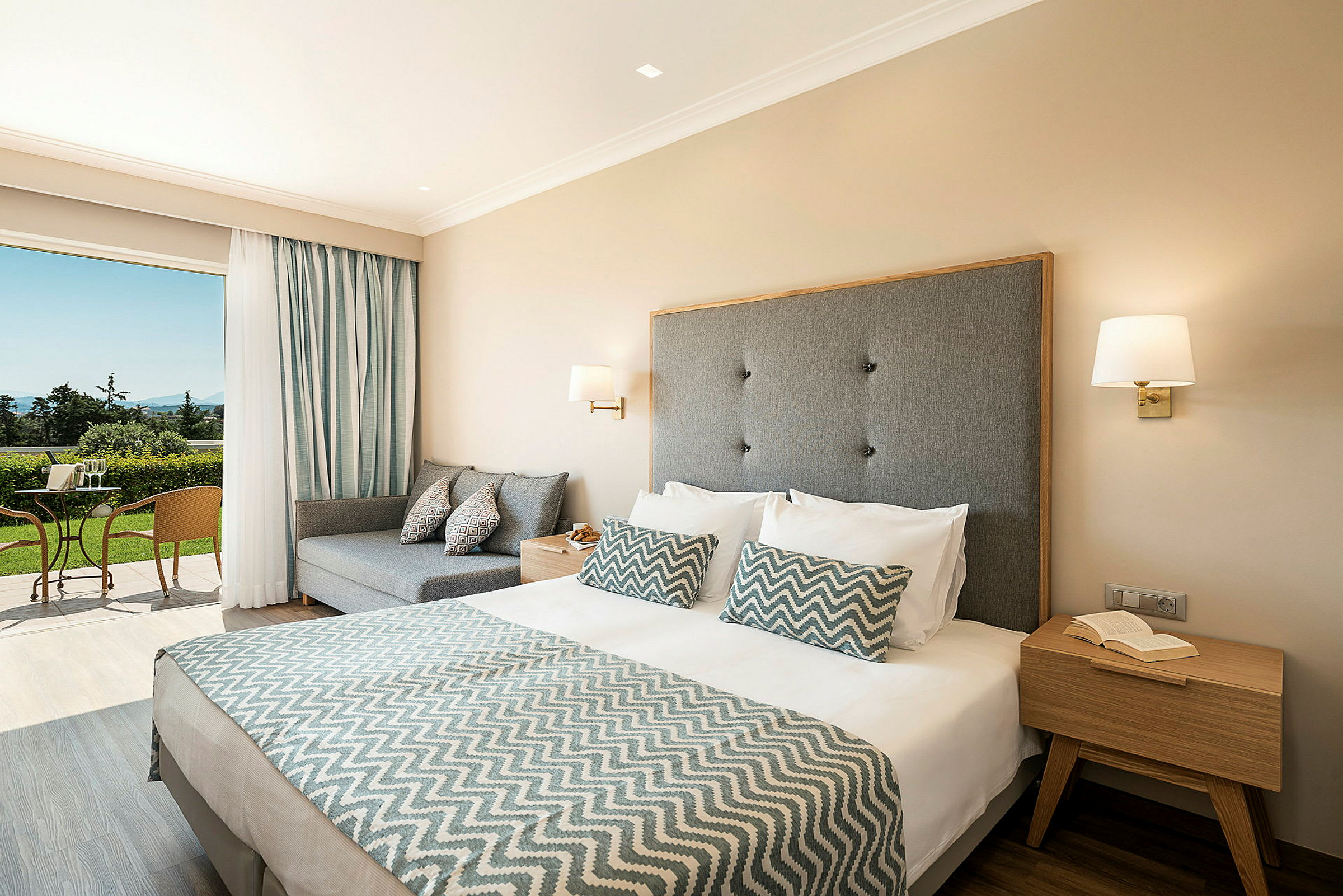 Hotellrum med dubbelsäng och sittgrupp, samt utgång till terrass med naturutsikt. (AI-genererad text)