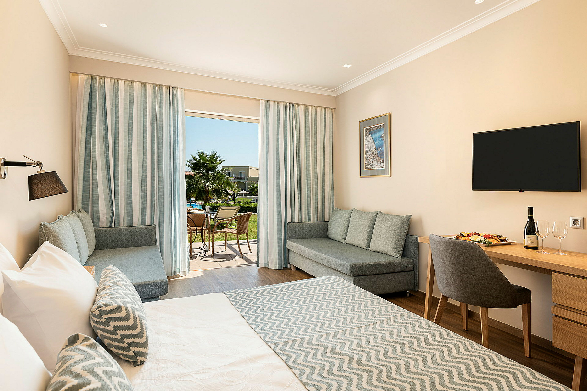 Ett hotellrum med en stor säng, sittgrupp och ett skrivbord. Uteplatsen syns genom glasdörrar. (AI-genererad text)