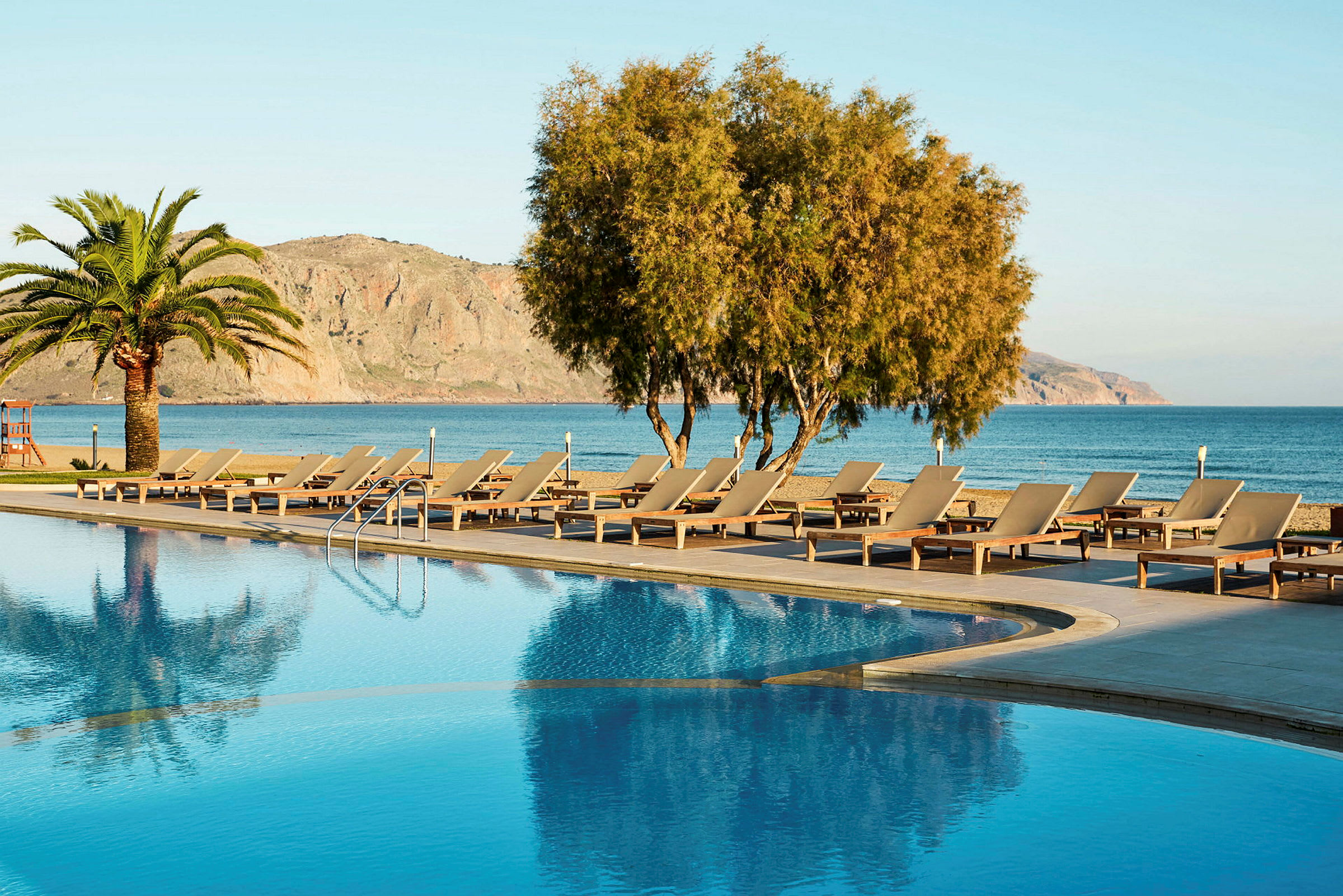 En pool med solstolar och utsikt över havet och berg. (AI-genererad text)