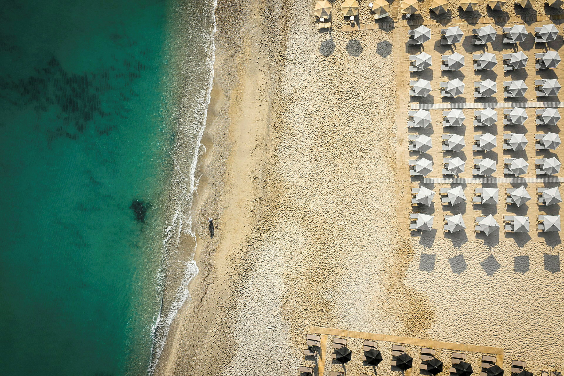 Strand med solparasoller och hav vid sidan. (AI-genererad text)