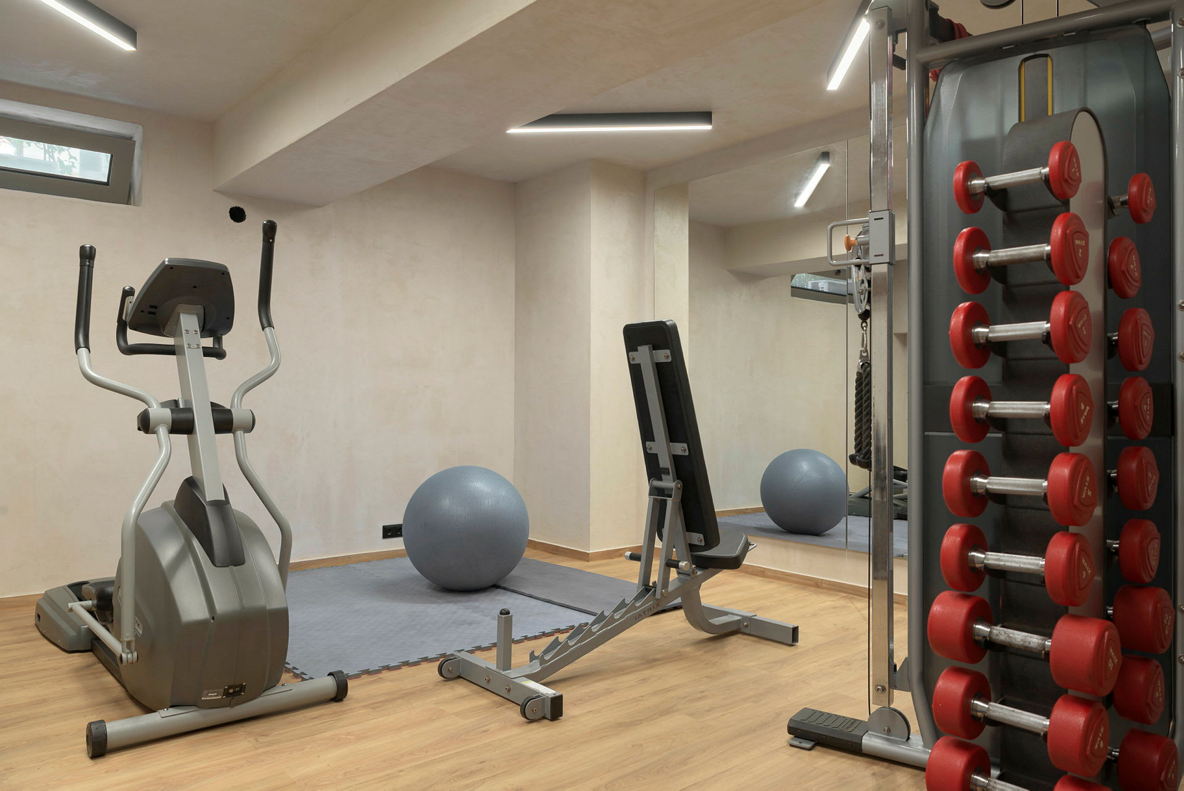 Gym med träningsmaskiner, bänk, hantlar och en grå träningsboll. (AI-genererad text)