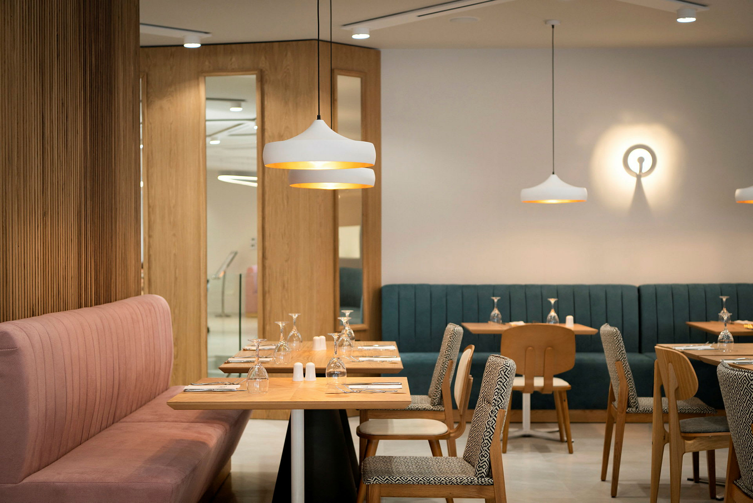 En modern restaurang med bord och stolar i trä, färgglada stoppade soffor och dekorativa ljusarmaturer. (AI-genererad text)