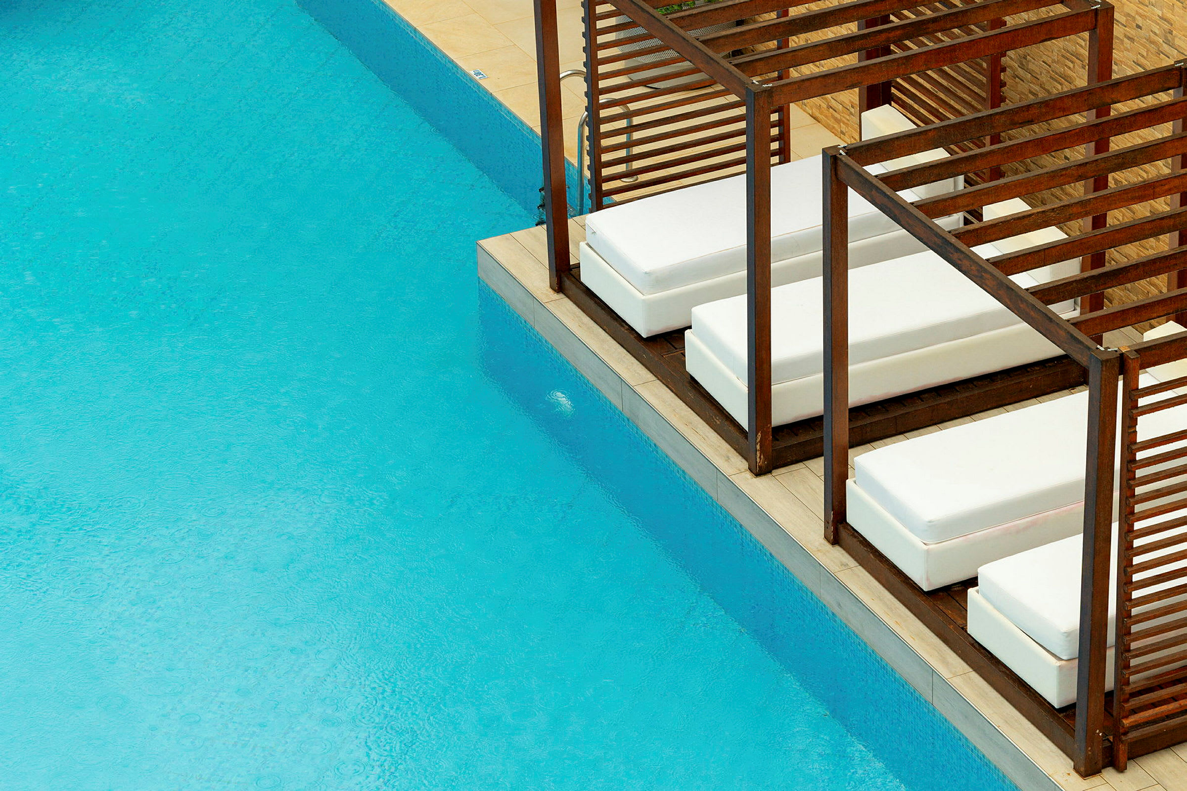 Loungemöbler med vita dynor vid en pool med blått vatten. (AI-genererad text)