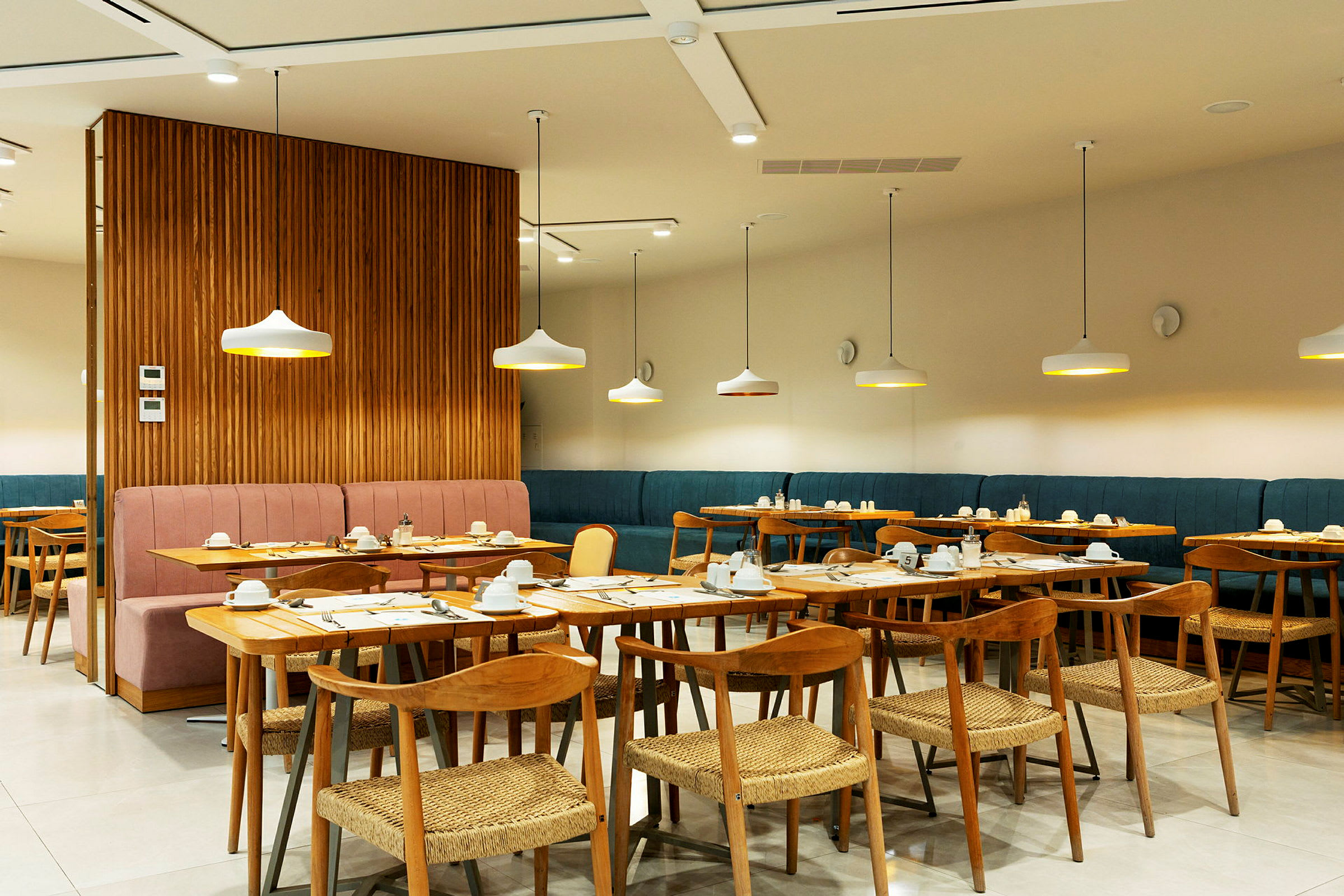 En modern inomhusrestaurang med bord och stolar i trä, samt stilfullt placerade taklampor. (AI-genererad text)