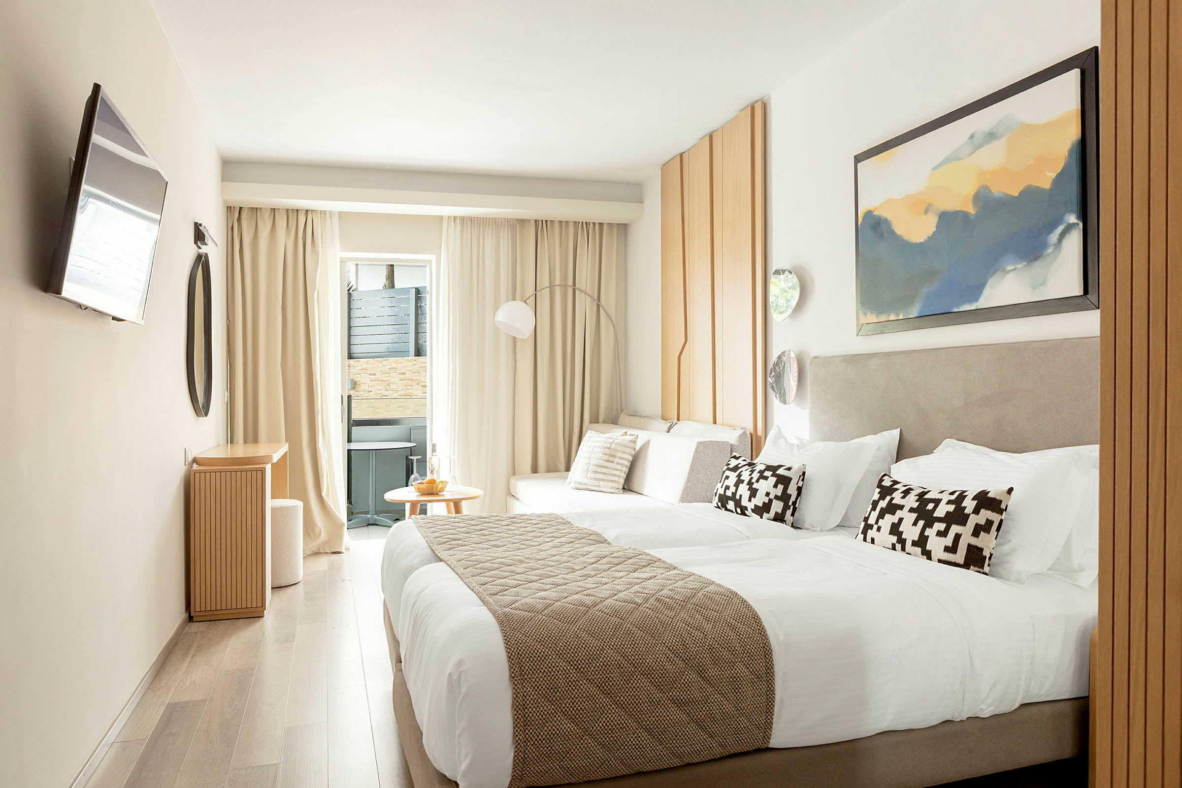 Ett modernt hotellrum med en dubbelsäng, ljusa möbler och dekorationer samt en liten sittgrupp nära ett fönster. (AI-genererad text)