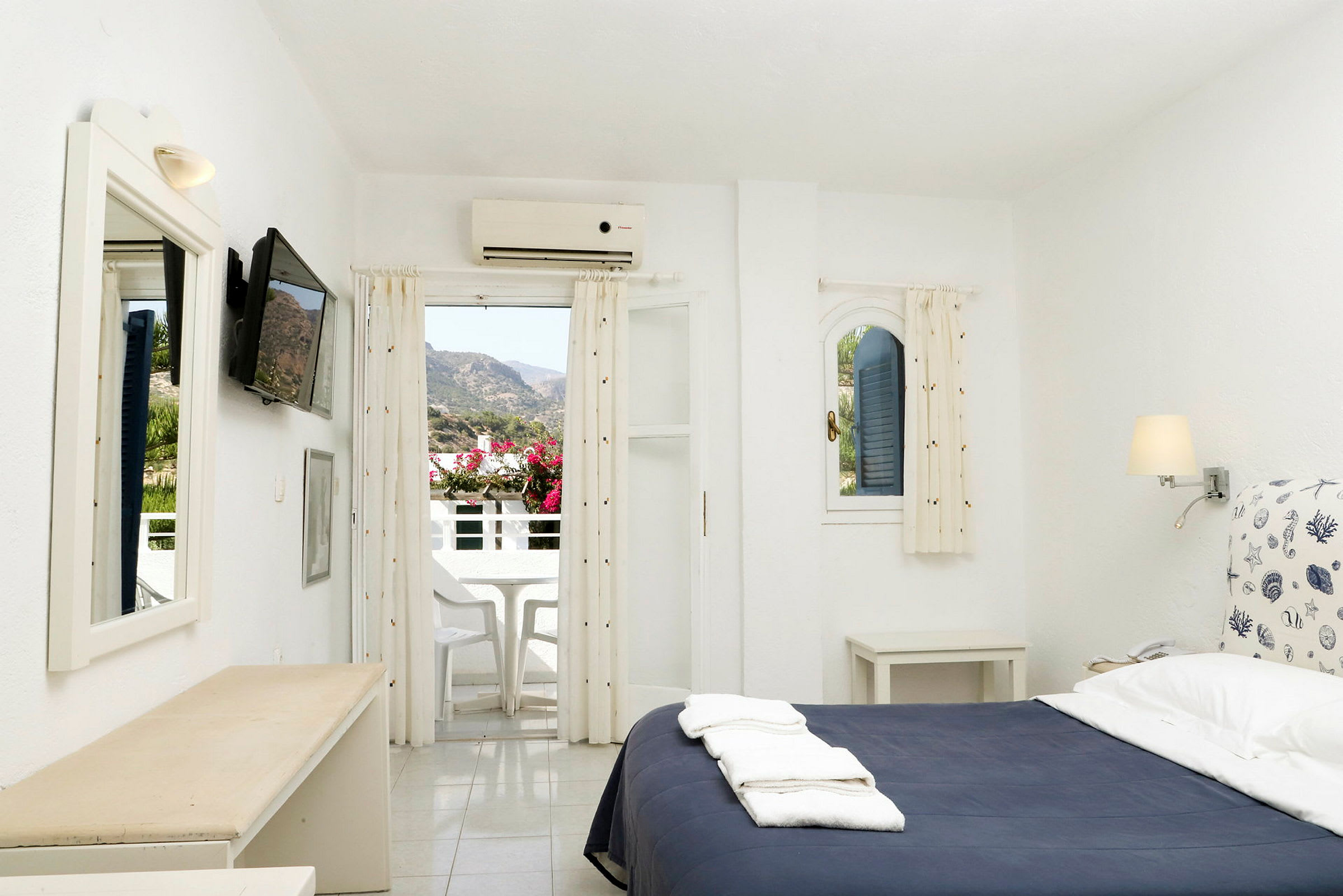 Ett hotellrum med en säng, en tv på väggen och en balkong som visar utsikt över bergen. (AI-genererad text)