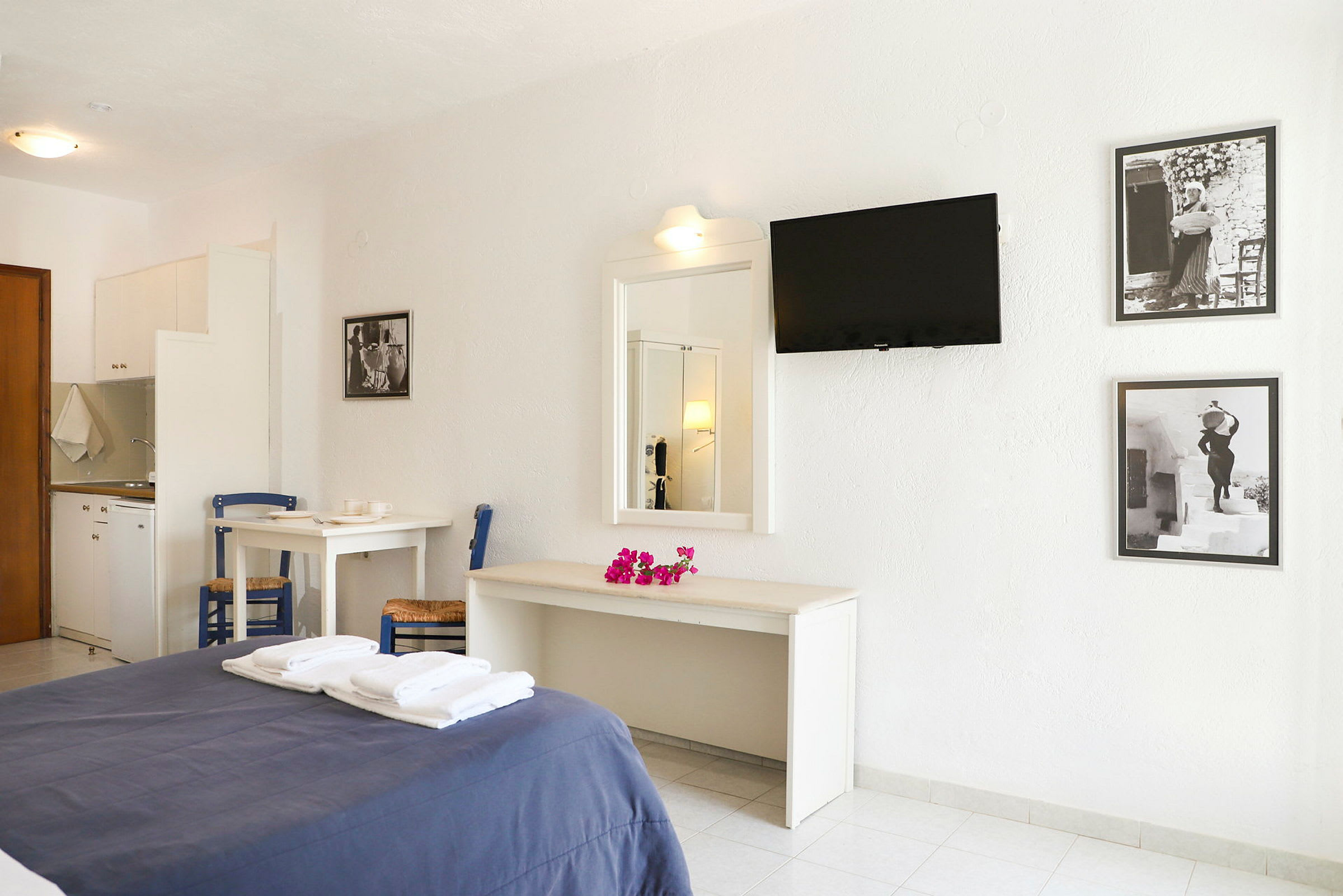 Ett hotellrum med en dubbelsäng, vita möbler, en väggmonterad TV och svartvita tavlor på väggen. (AI-genererad text)