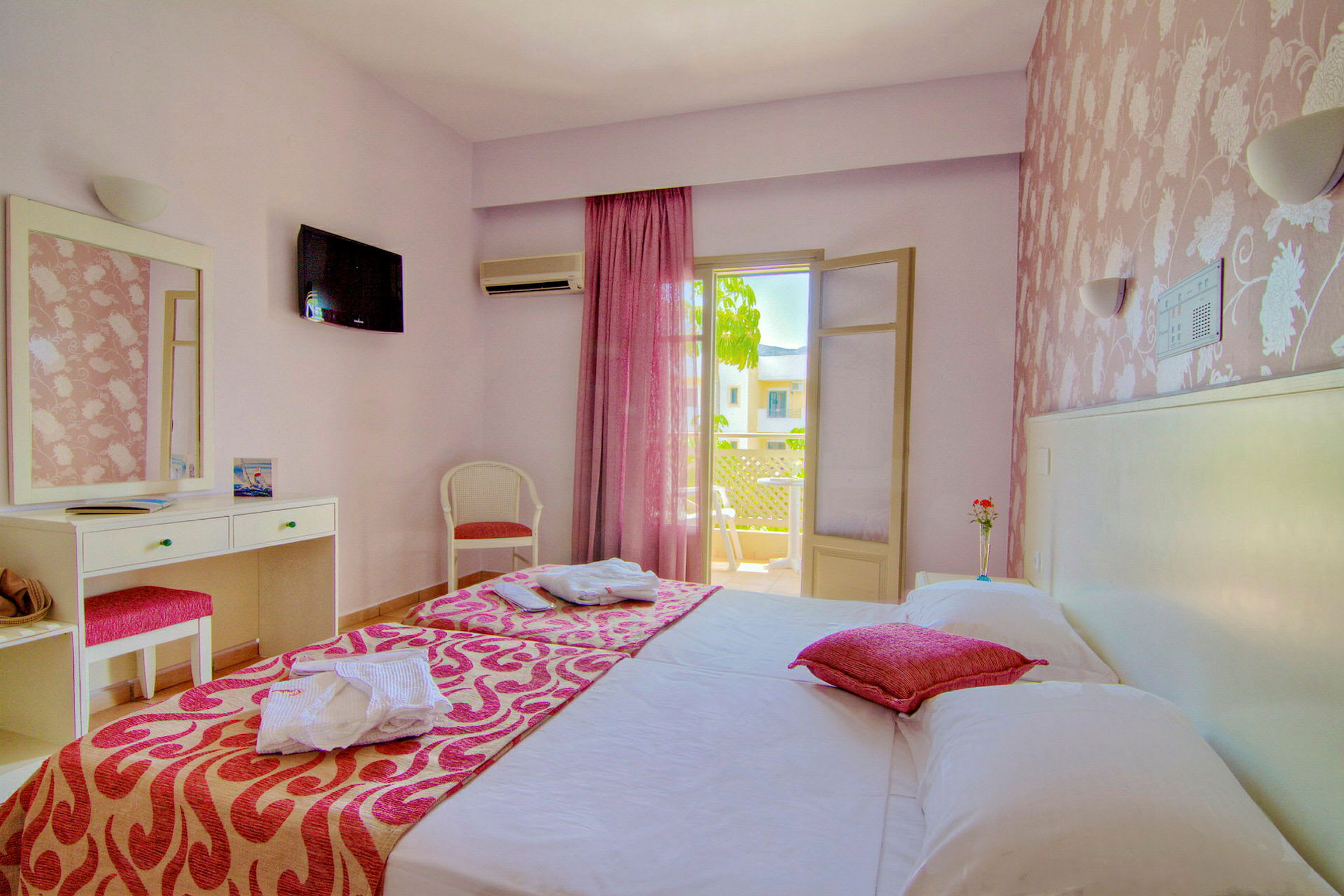 Ett ljust hotellrum med dubbelsäng, rosa detaljer och en balkong. (AI-genererad text)