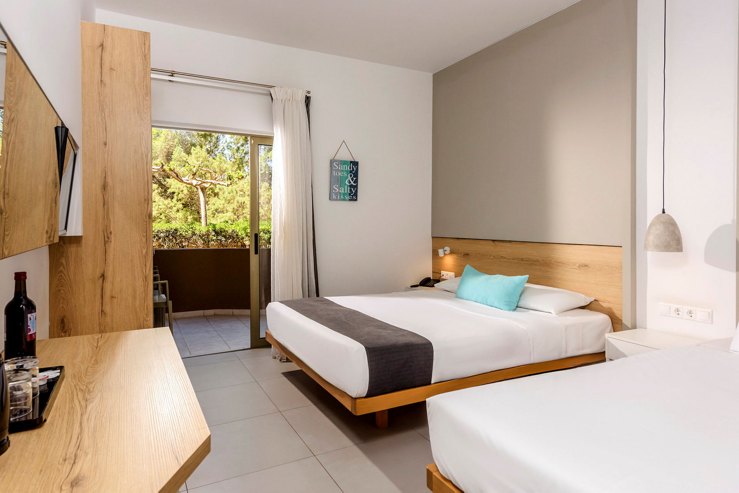 Ett hotellrum med två sängar, ljusa trämöbler och en balkong med grön utsikt. (AI-genererad text)