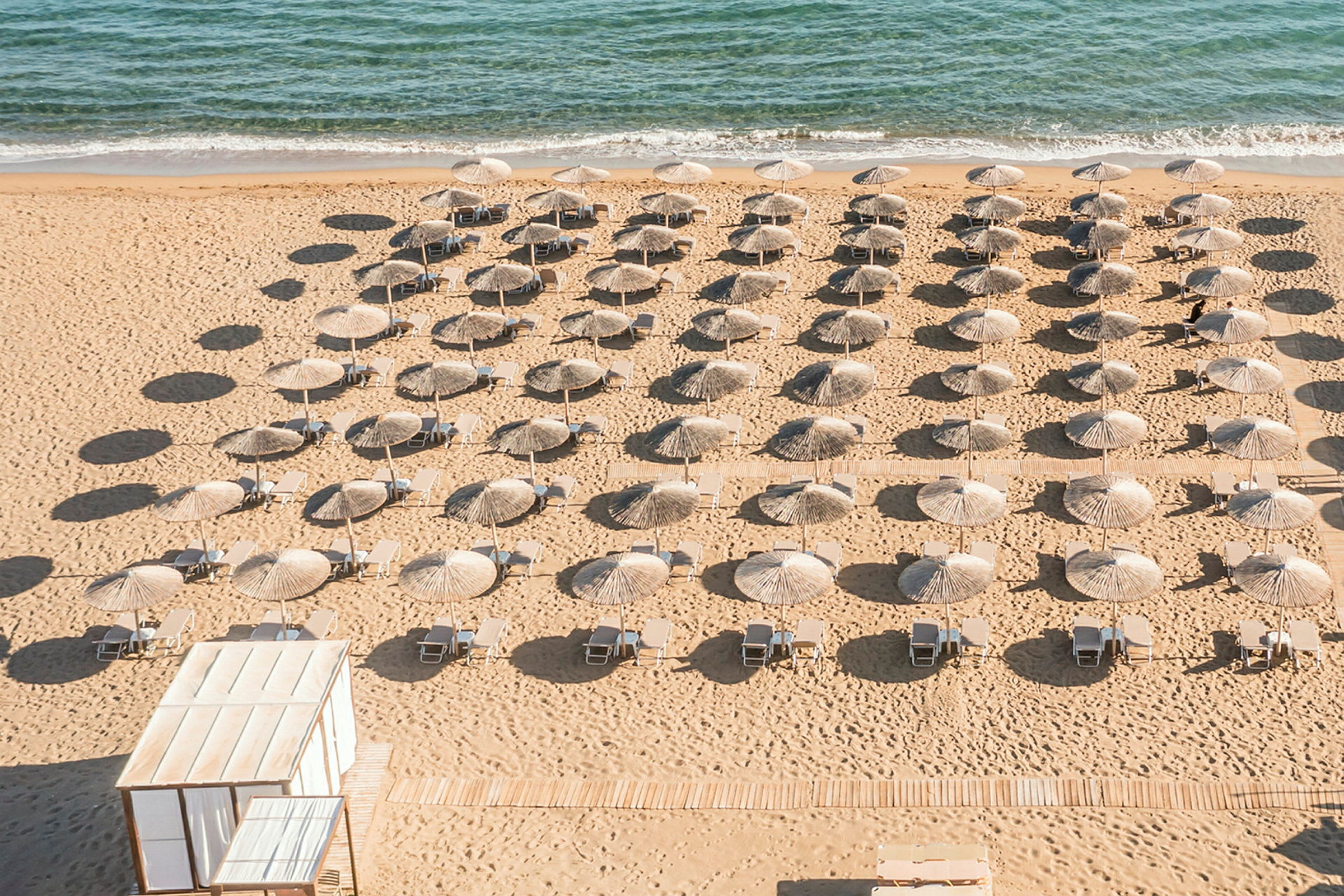 Strand med parasoller och solstolar i rader framför havet. (AI-genererad text)